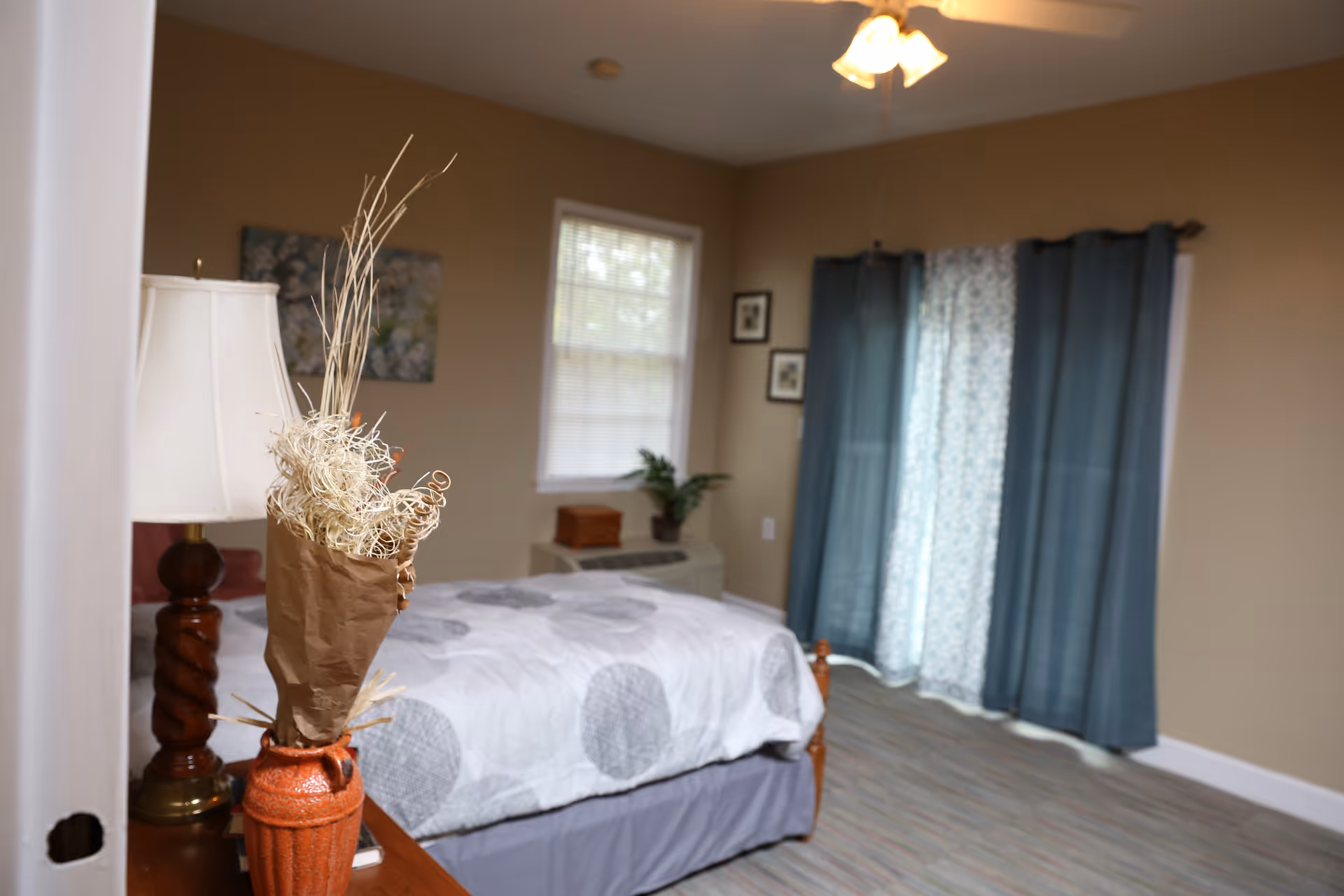 Decorated bedroom with a bed, lamp, curtains, and nightstand in neutral tones.