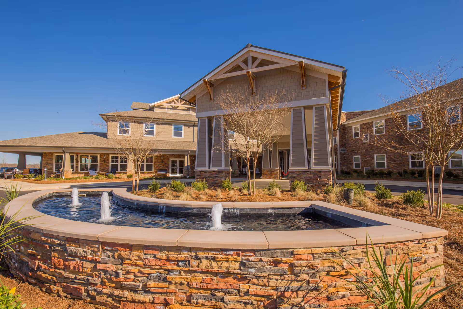 Front entrance of a senior living building with a circular stone fountain and covered porte-cochère.