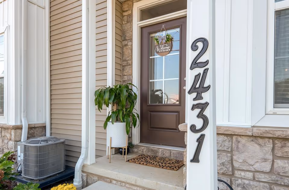 Front entry of a senior living facility with a brown door, house numbers, and potted plant.