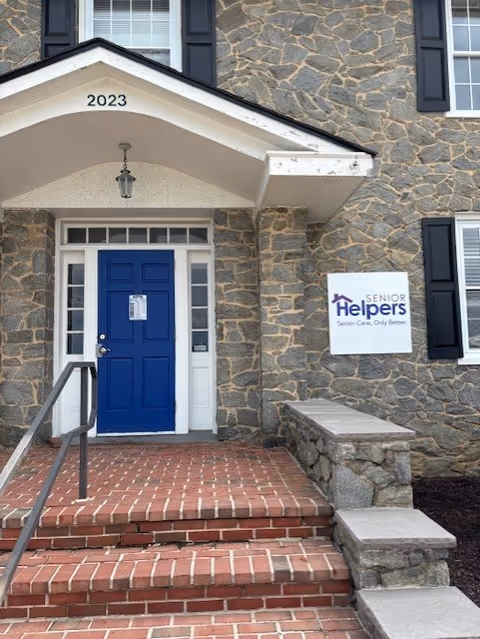 Stone faced building entrance with blue door, steps, and Senior Helpers sign.