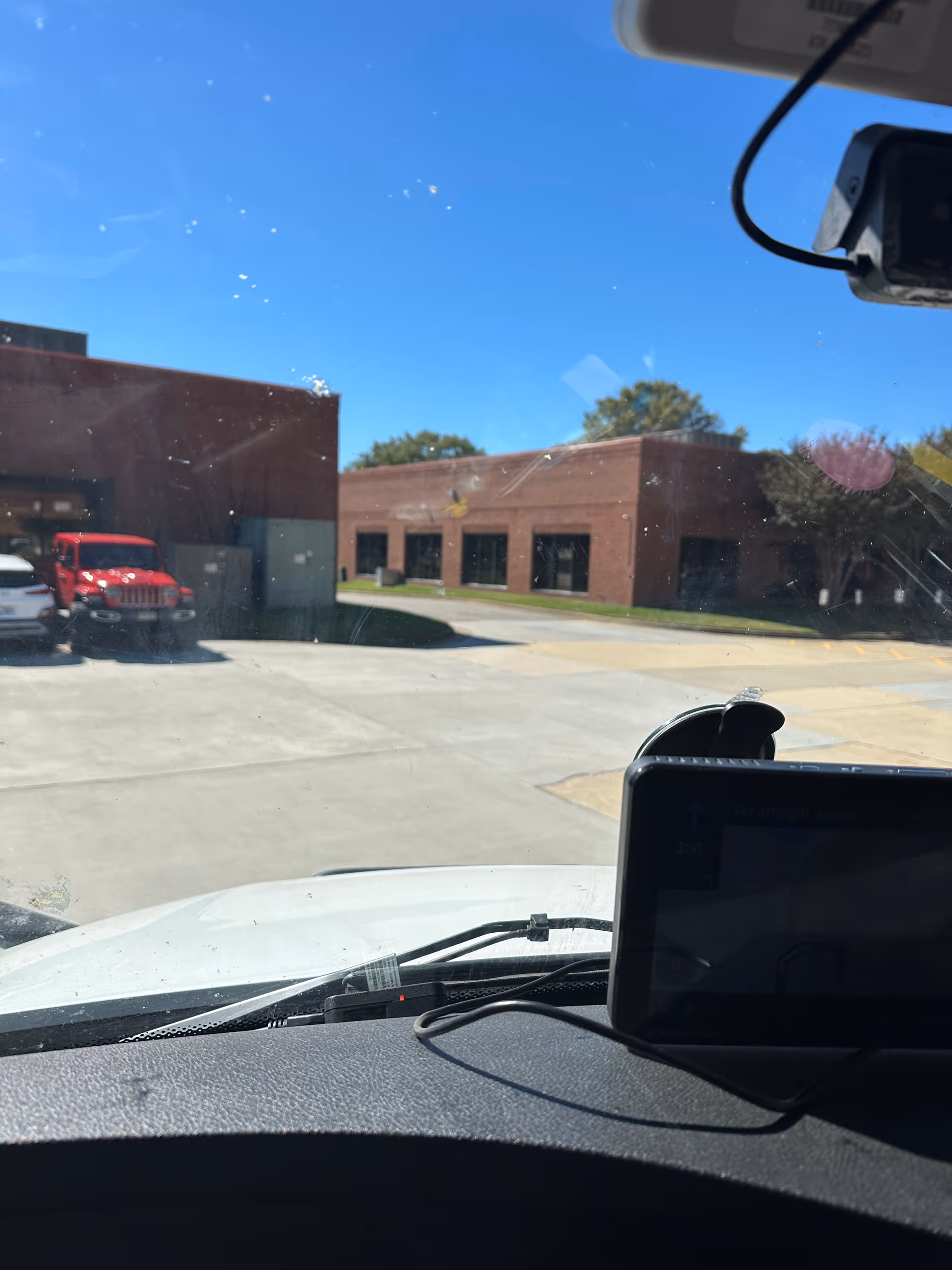 Vehicle dashboard view of Sentara Home Care Services building exterior with brick facade and parking lot.