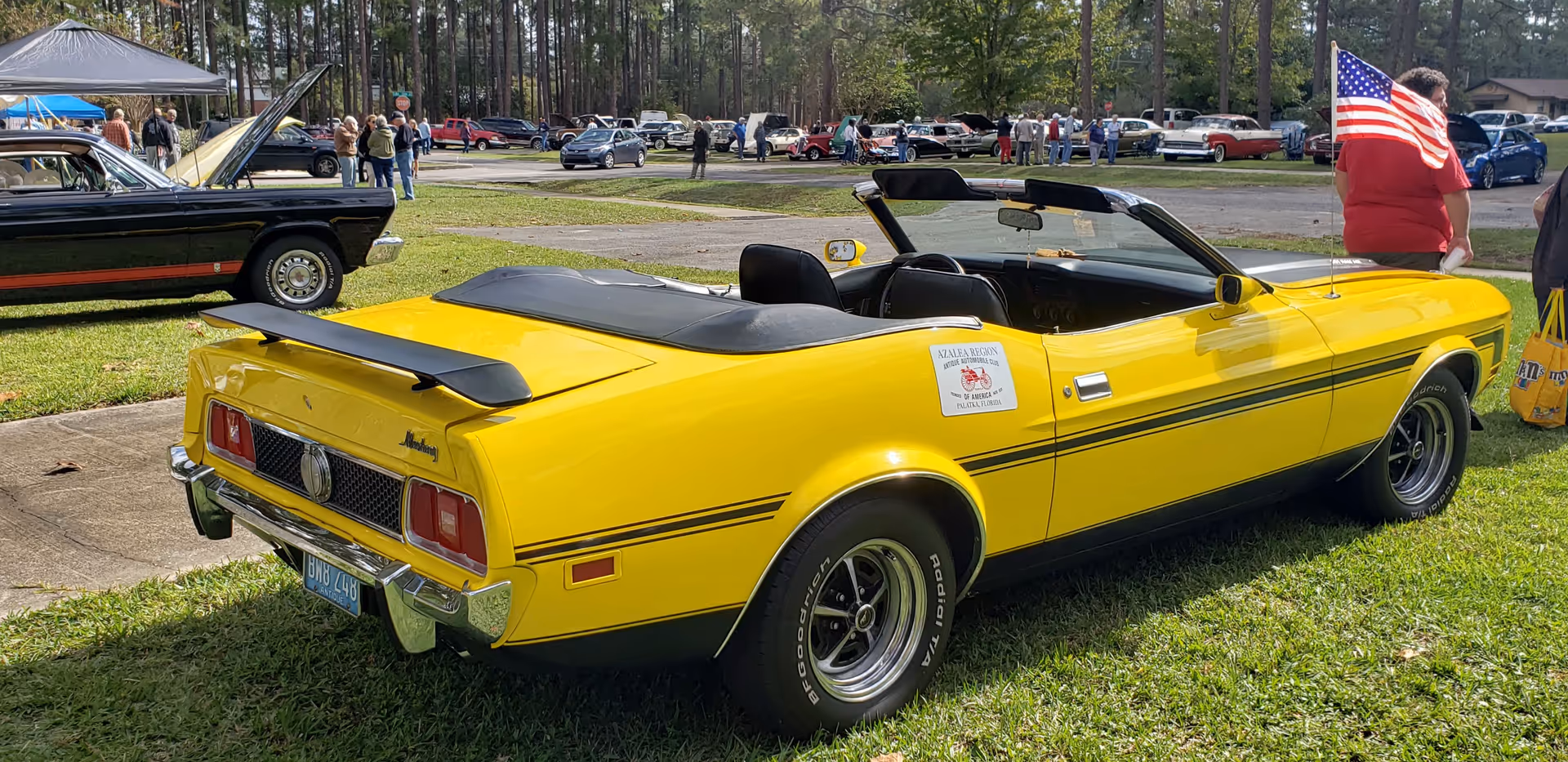 A bright yellow convertible car parked on grass at an outdoor car show.