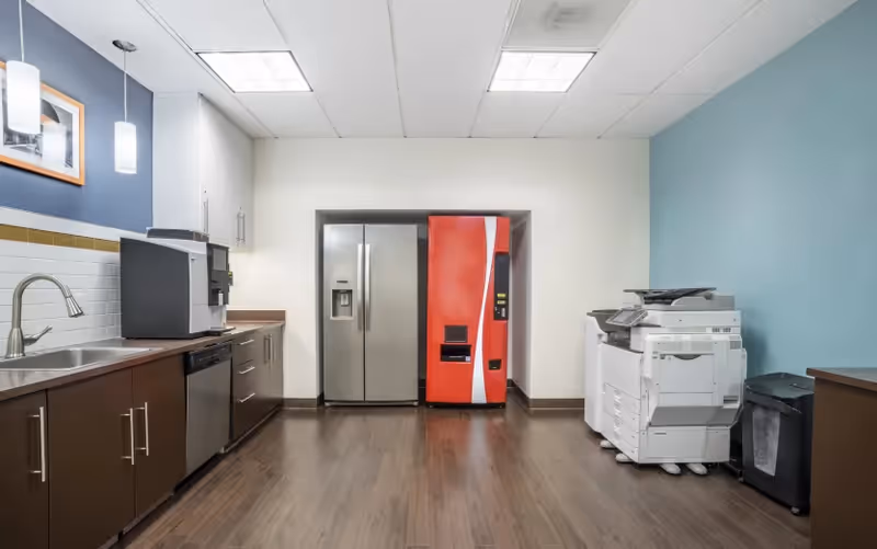 Kitchen area in a senior living facility featuring fridge, coffee station, and copier.