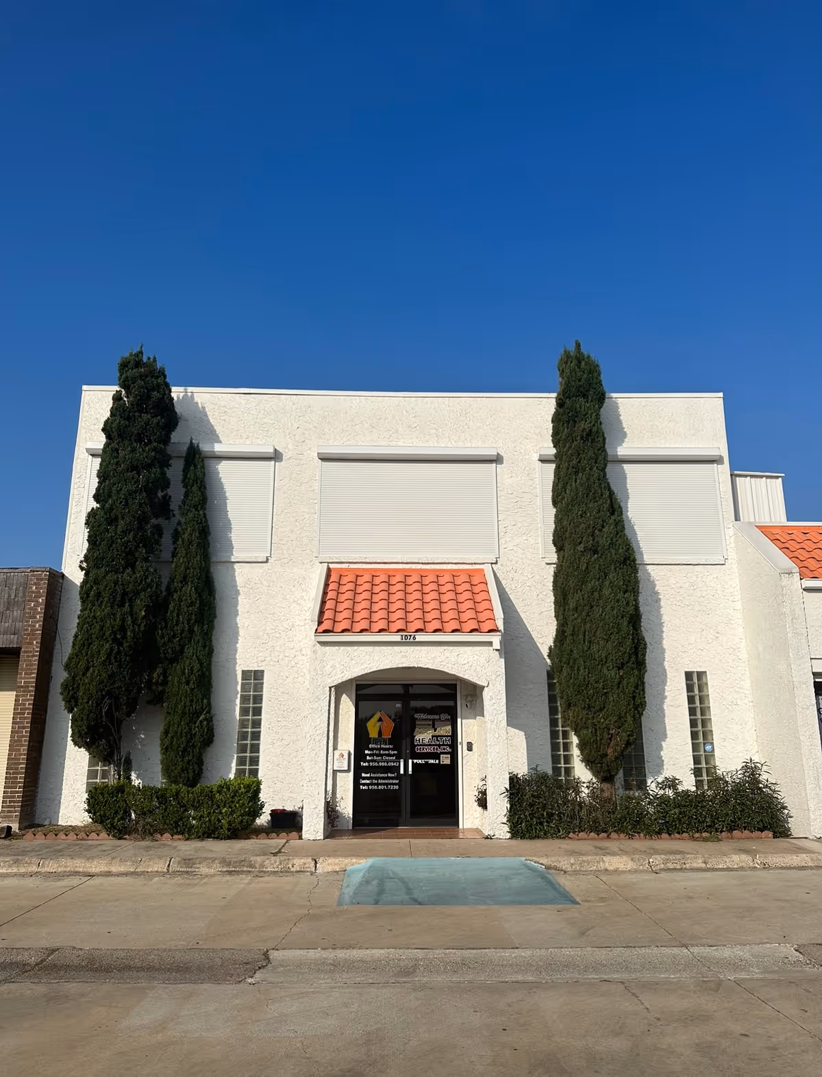 Entrance of Acclaim Health Services, Inc. building with red-tiled awning and tall evergreens.