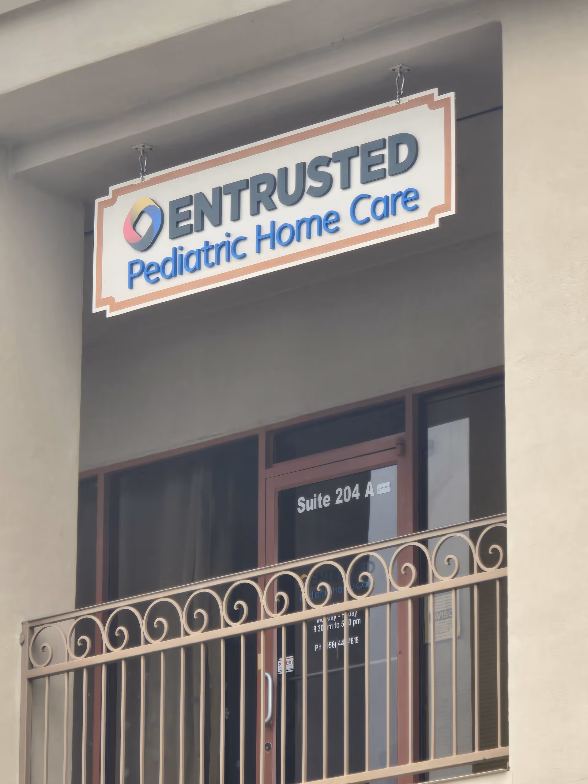 Exterior view of a building shows a sign reading Entrusted Pediatric Home Care above a balcony.