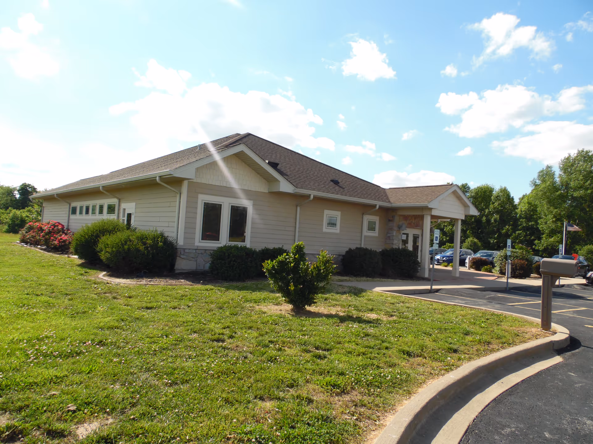 Single-story beige building with front entrance, parking lot, and well-kept landscaping.