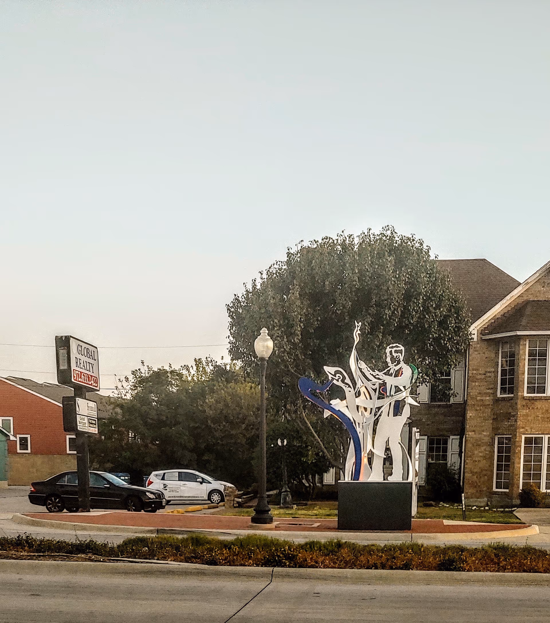 Outdoor street view featuring a circular driveway and a modern sculpture.