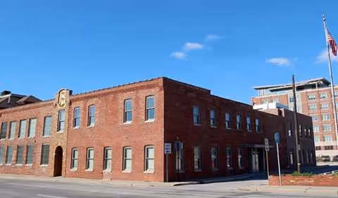 Brick building exterior along a street with blue sky above and sidewalk.
