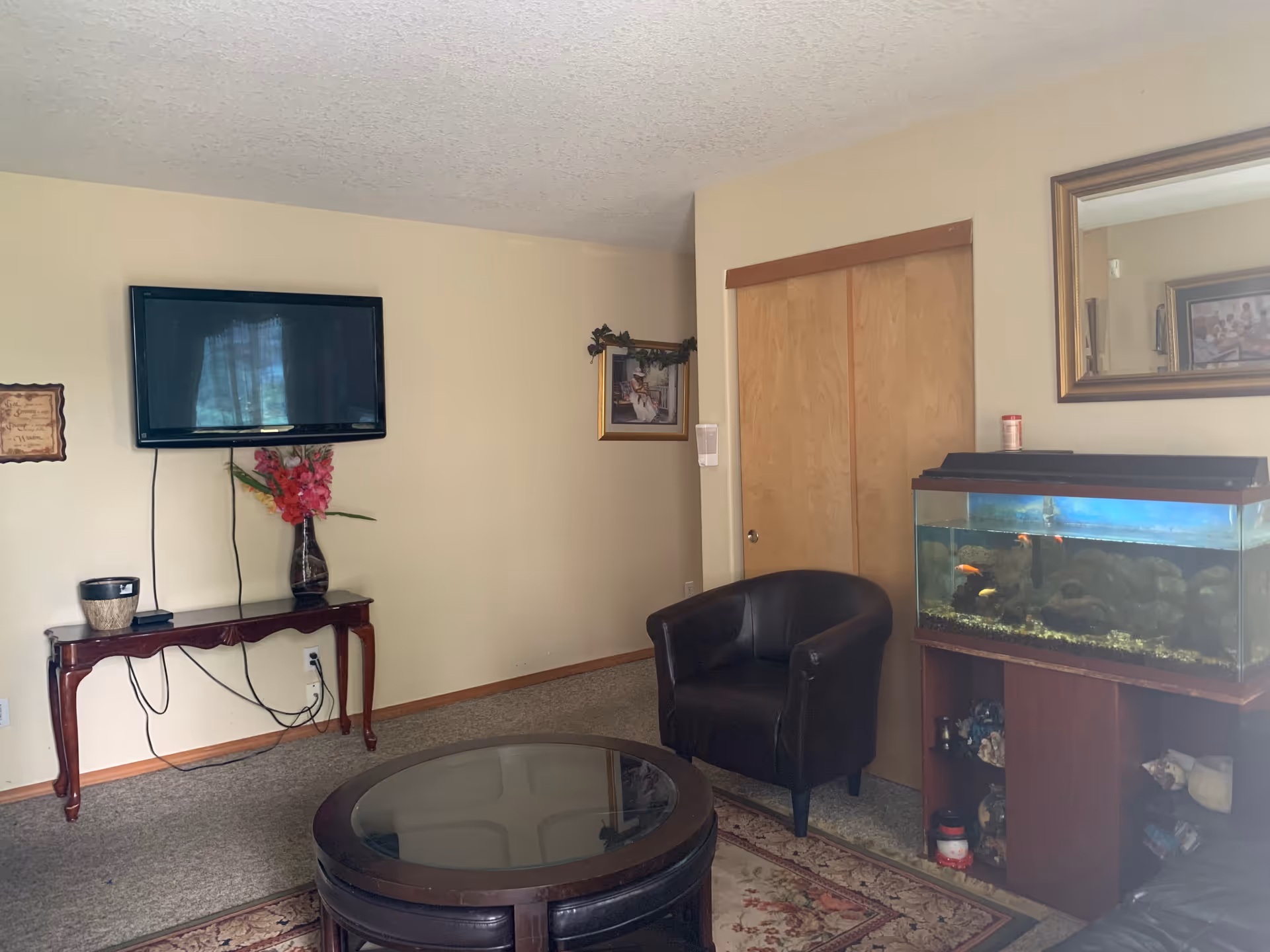 Cozy living room with wall-mounted TV, leather chairs, aquarium, and coffee table.