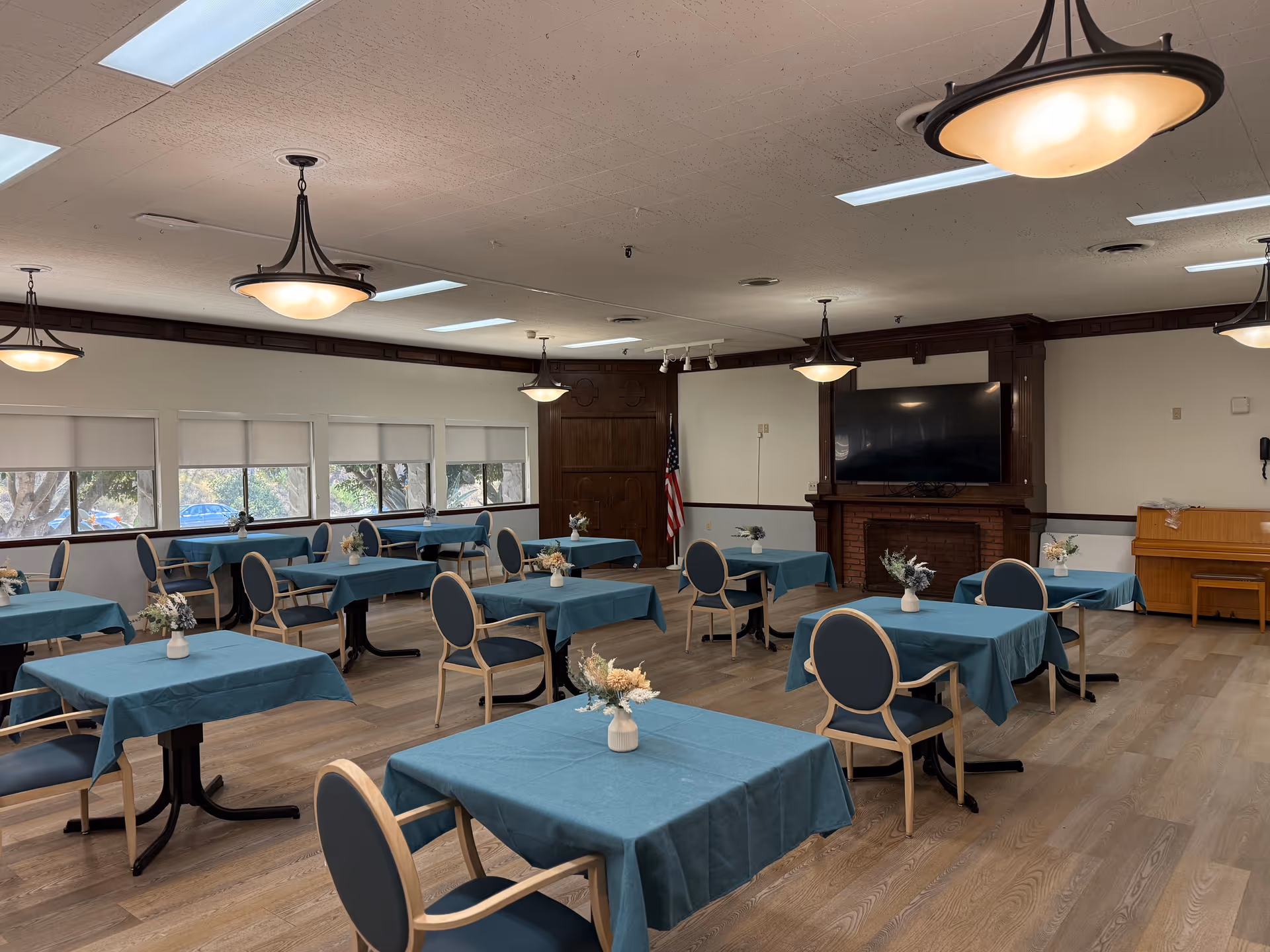 Dining room with teal tablecloths, blue chairs, and a TV above the fireplace.