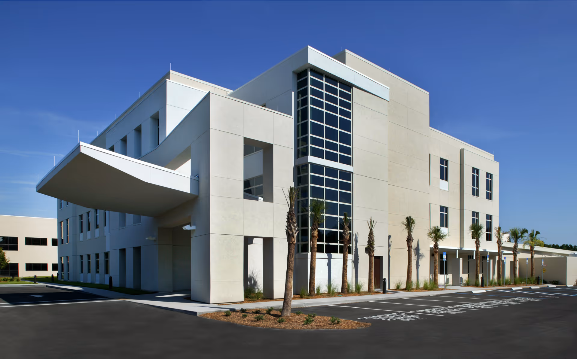 Modern beige hospice building exterior with palm trees and a parking lot.