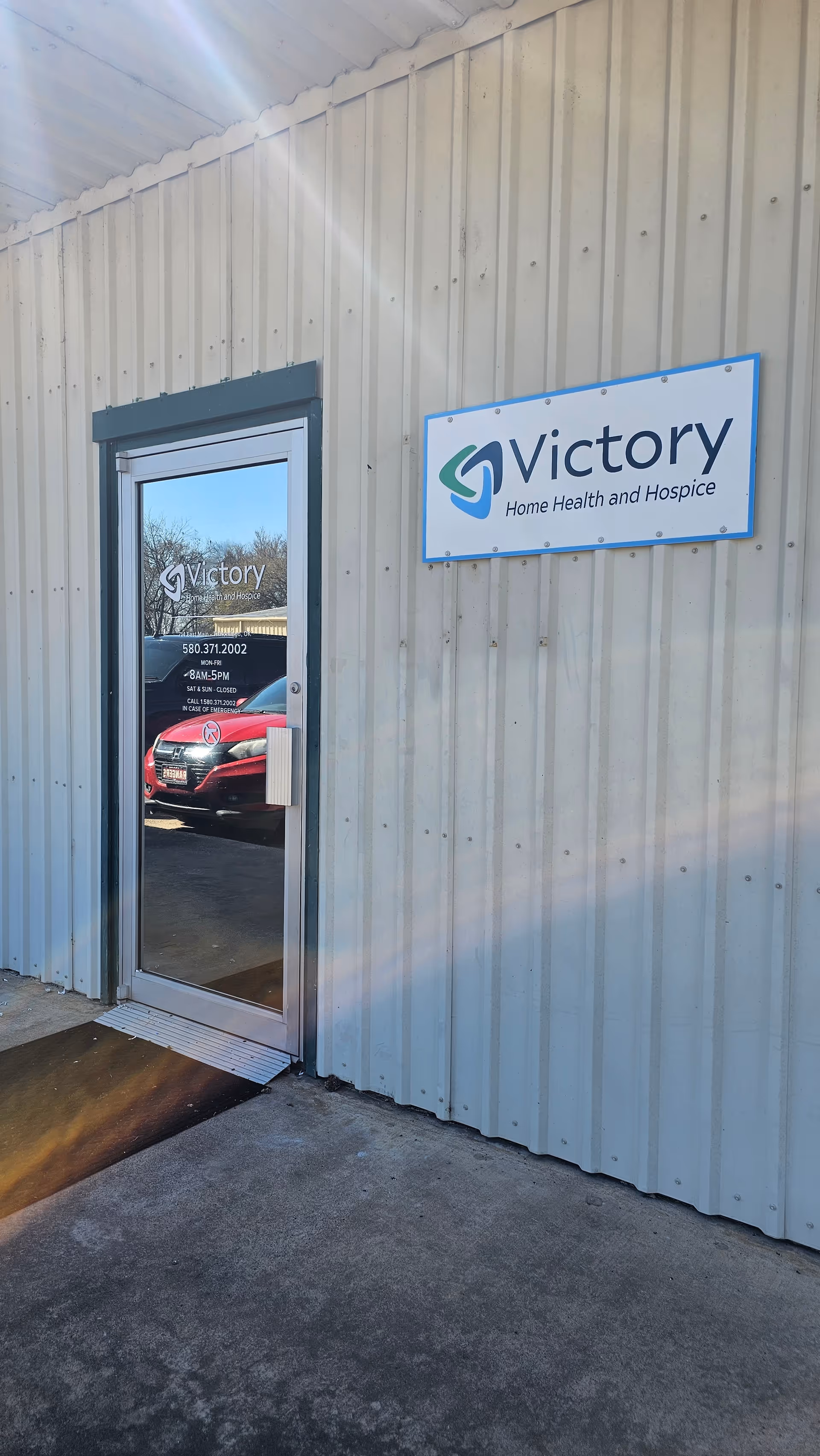 Exterior entrance of Victory Home Health and Hospice with blue sign on metal siding.