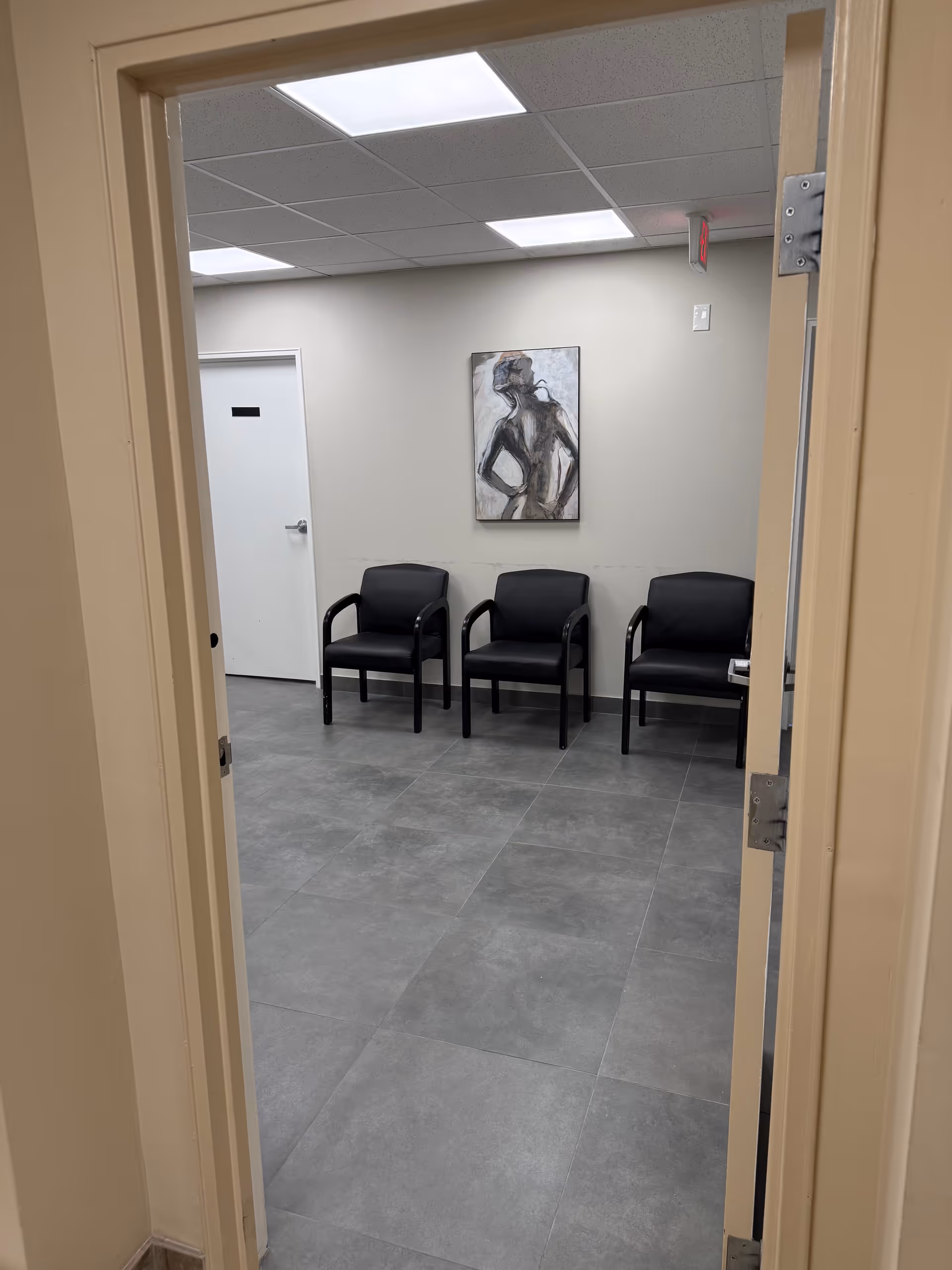 Interior waiting area with three black chairs and abstract painting.