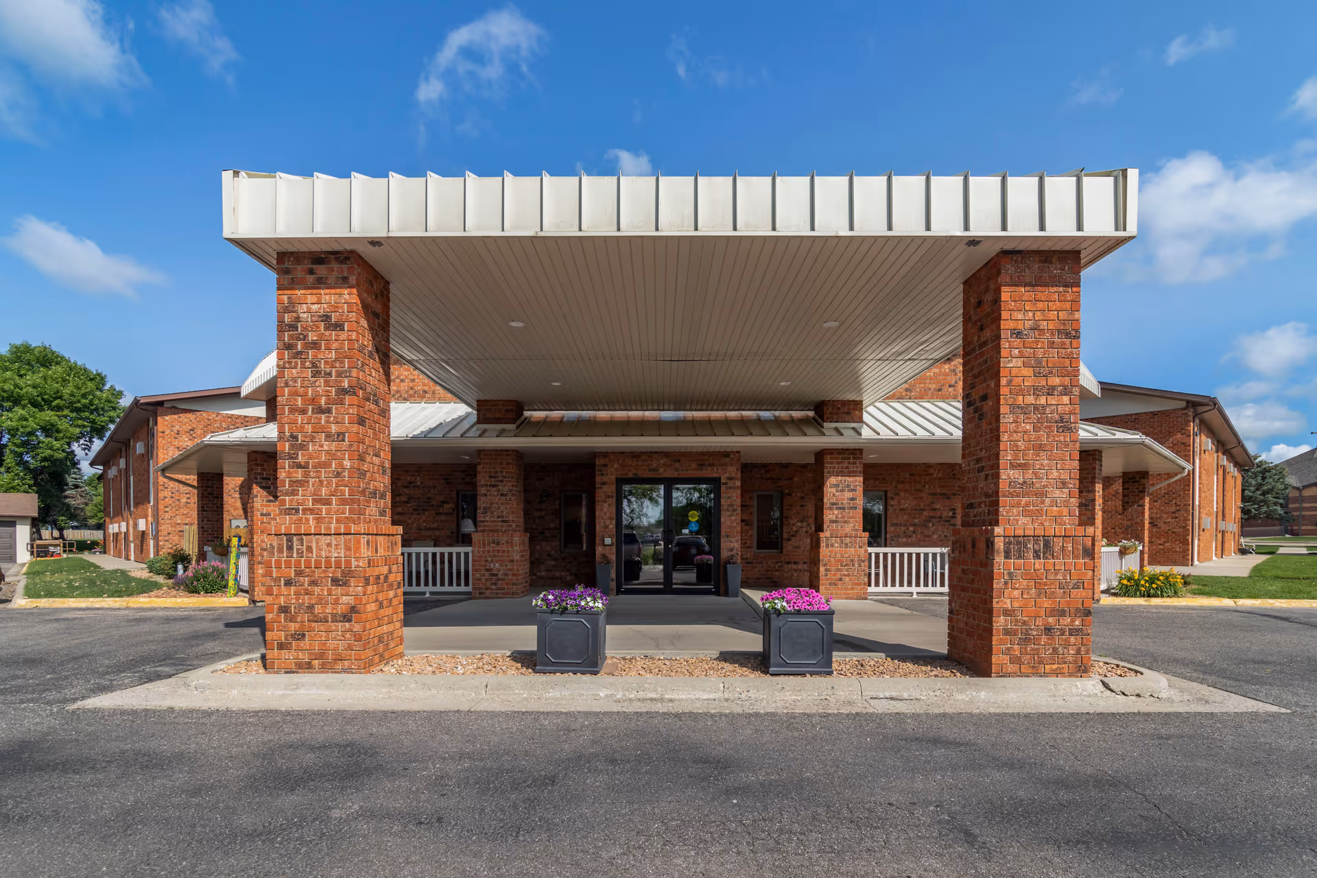 Brick senior living facility entrance with a large covered drive and planters.