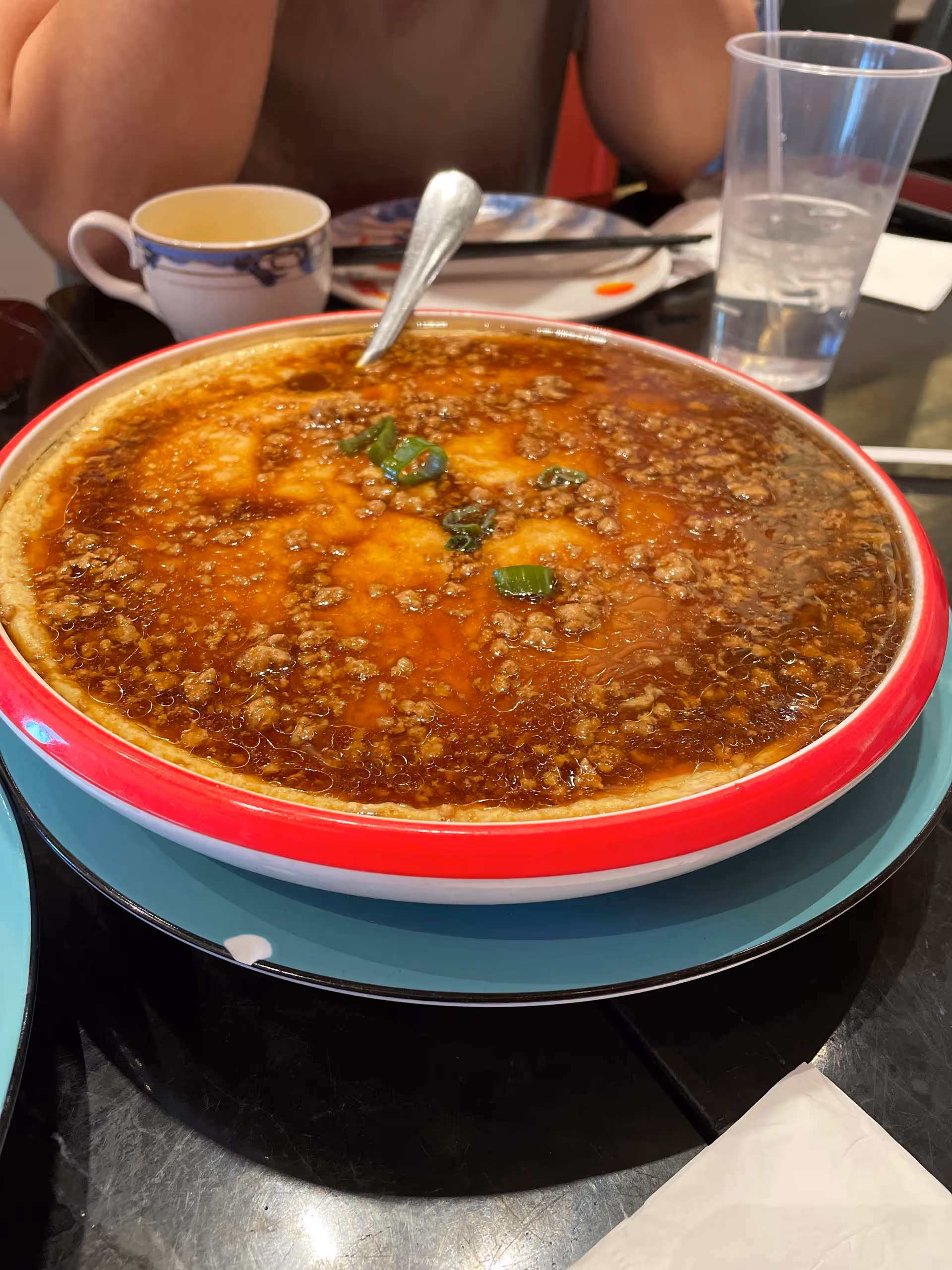 Close-up of a large saucy meat dish in a red-rimmed bowl on a dining table.