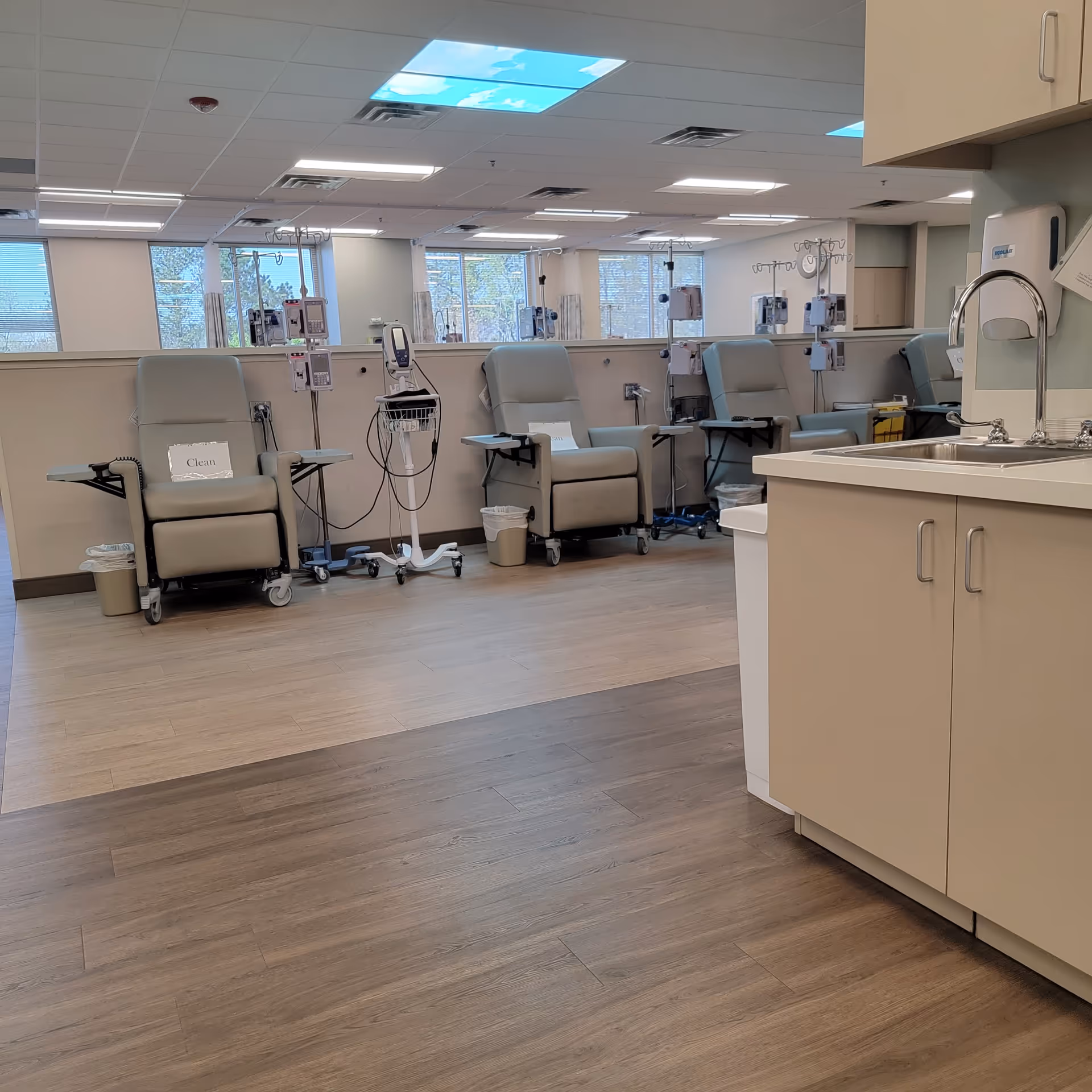 Beige recliners with IV poles line a bright infusion room in a medical facility.