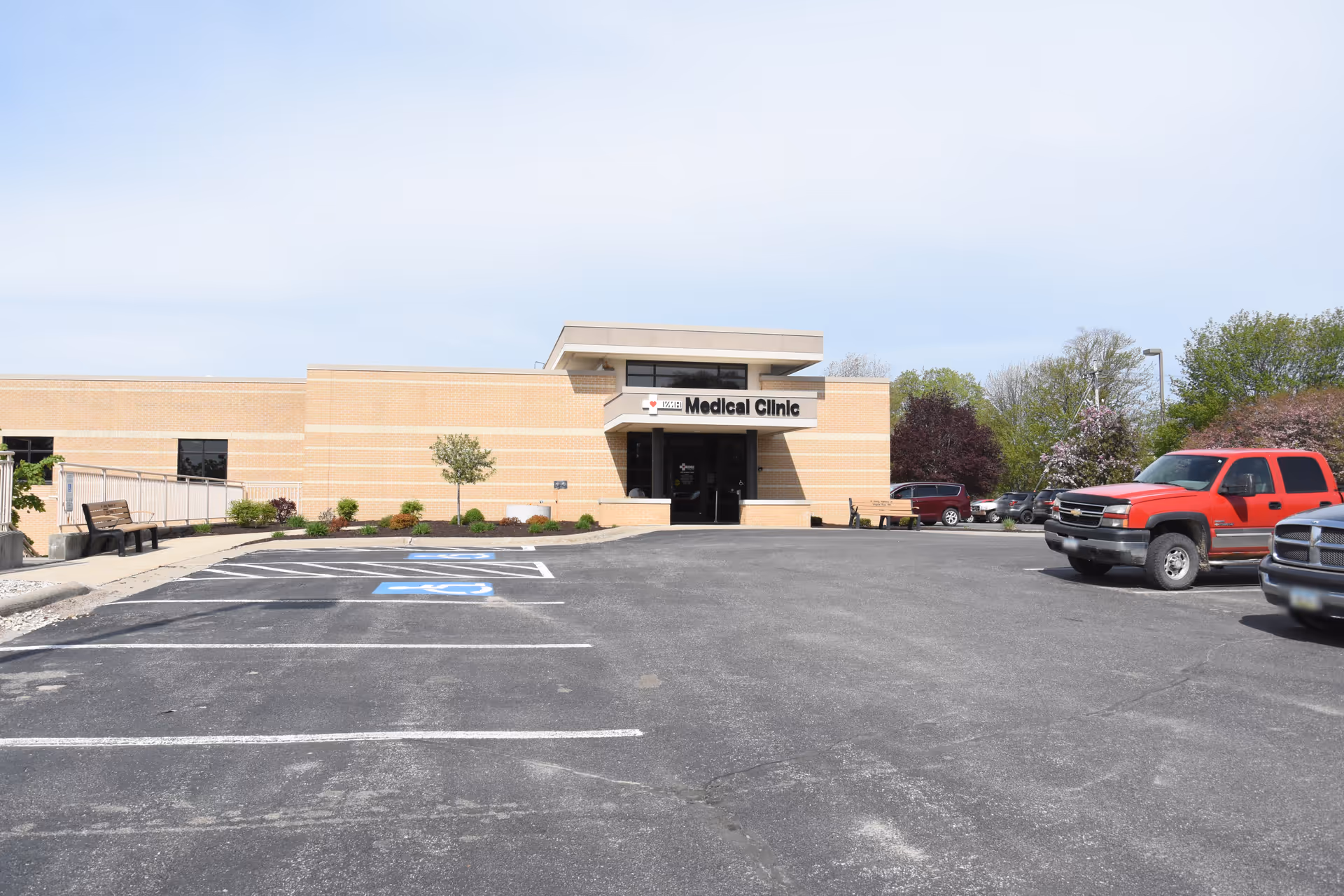 Exterior view of a beige brick medical facility with a parking lot in front.