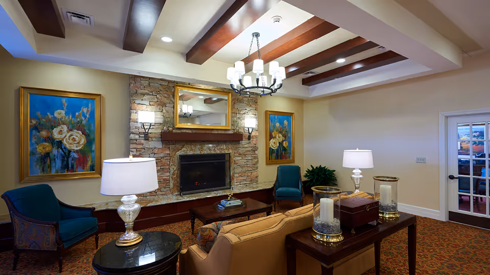 Cozy senior living lounge with fireplace, stone mantle, artwork, chandeliers, and seating.