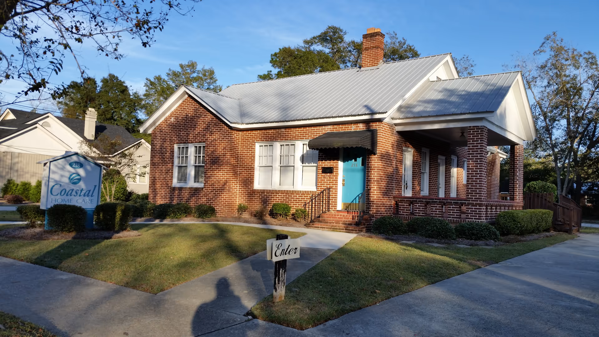Brick facility with teal entrance, Coastal Home Care sign, and manicured lawn.
