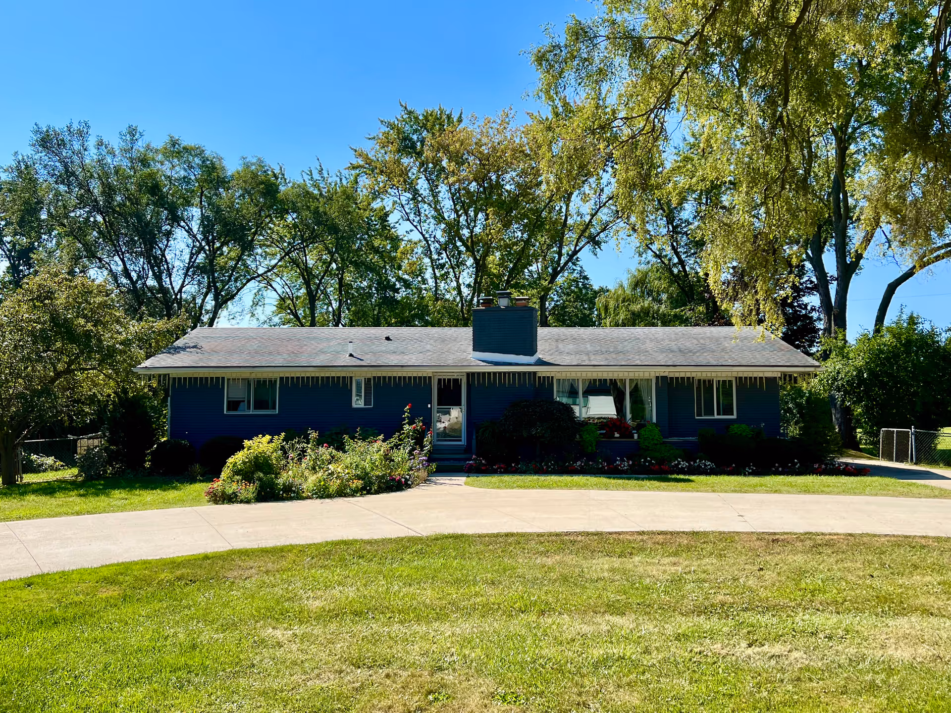 A blue single-story house with a front garden and driveway under a clear sky