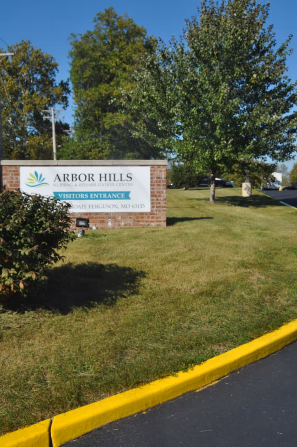 Brick entrance sign reading "Arbor Hills Nursing & Rehabilitation Center" on a grassy lawn with trees and a driveway curb.