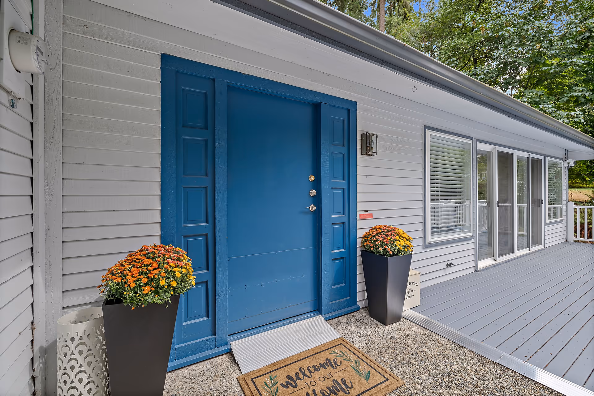 Blue front door with decorative panels and potted flowers on a gray exterior porch.