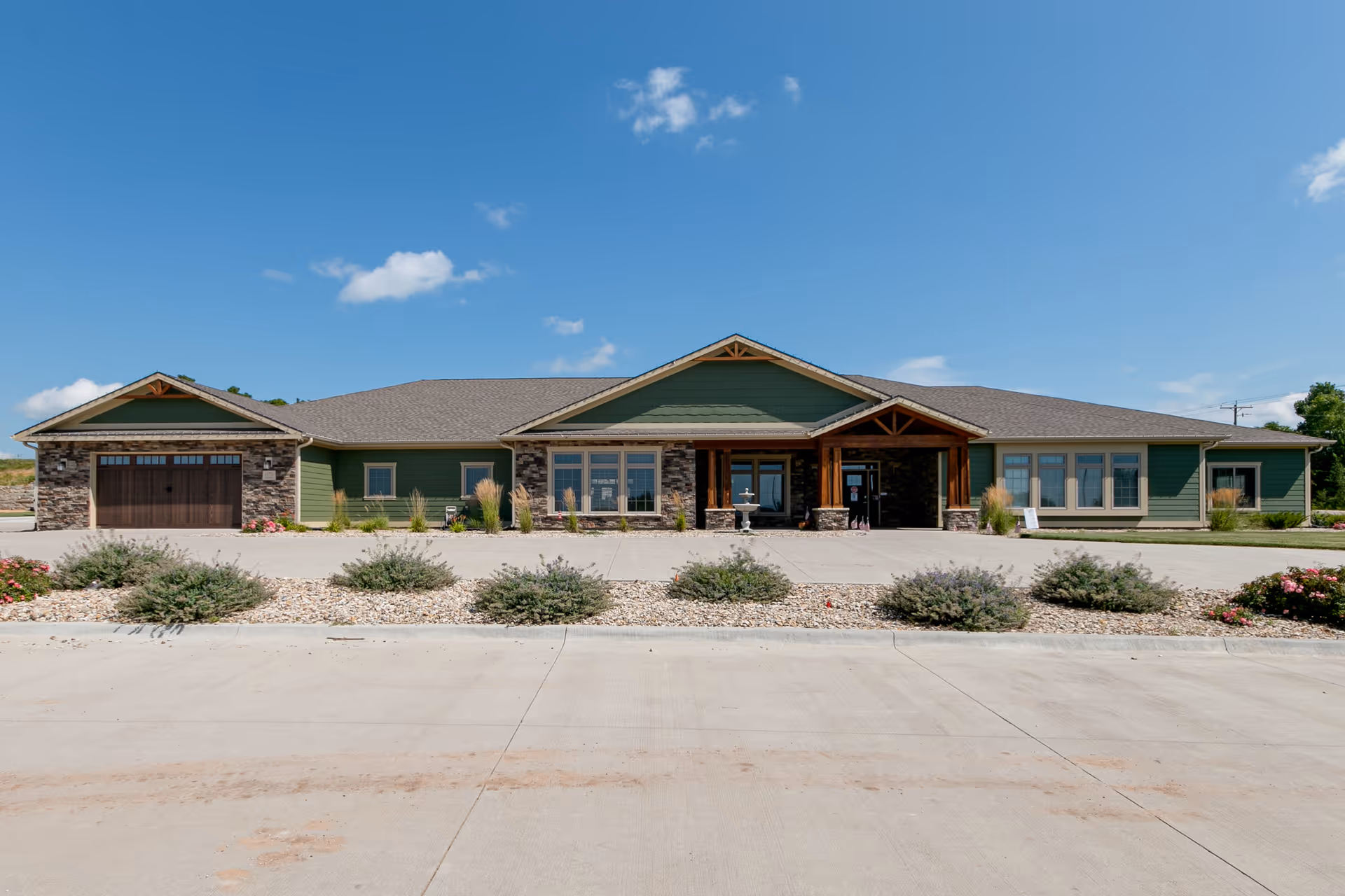 Front view of a green, single-story senior living facility with stone accents and a large entrance.