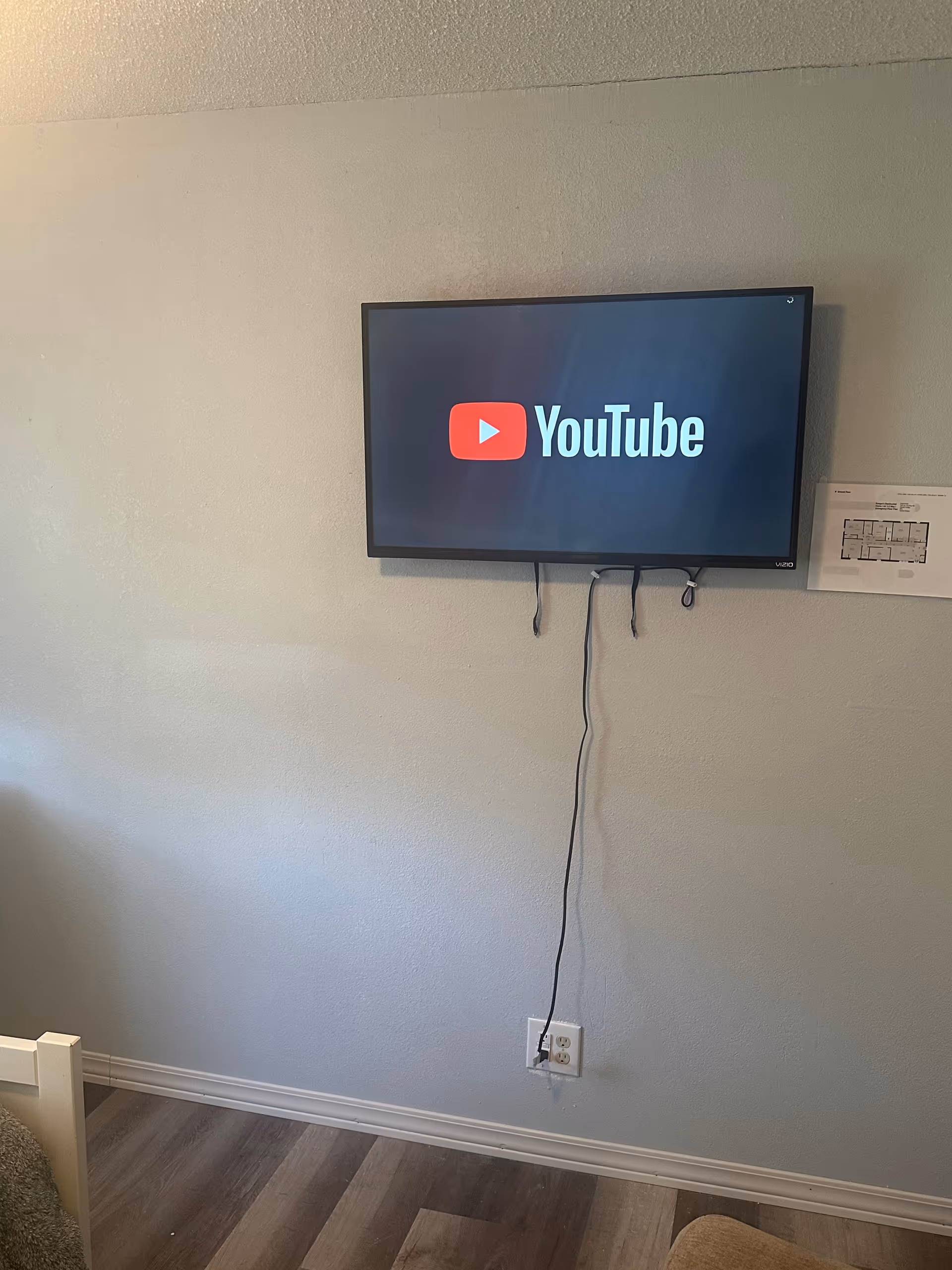 Wall-mounted TV shows YouTube in a bedroom with cords and wood floor.