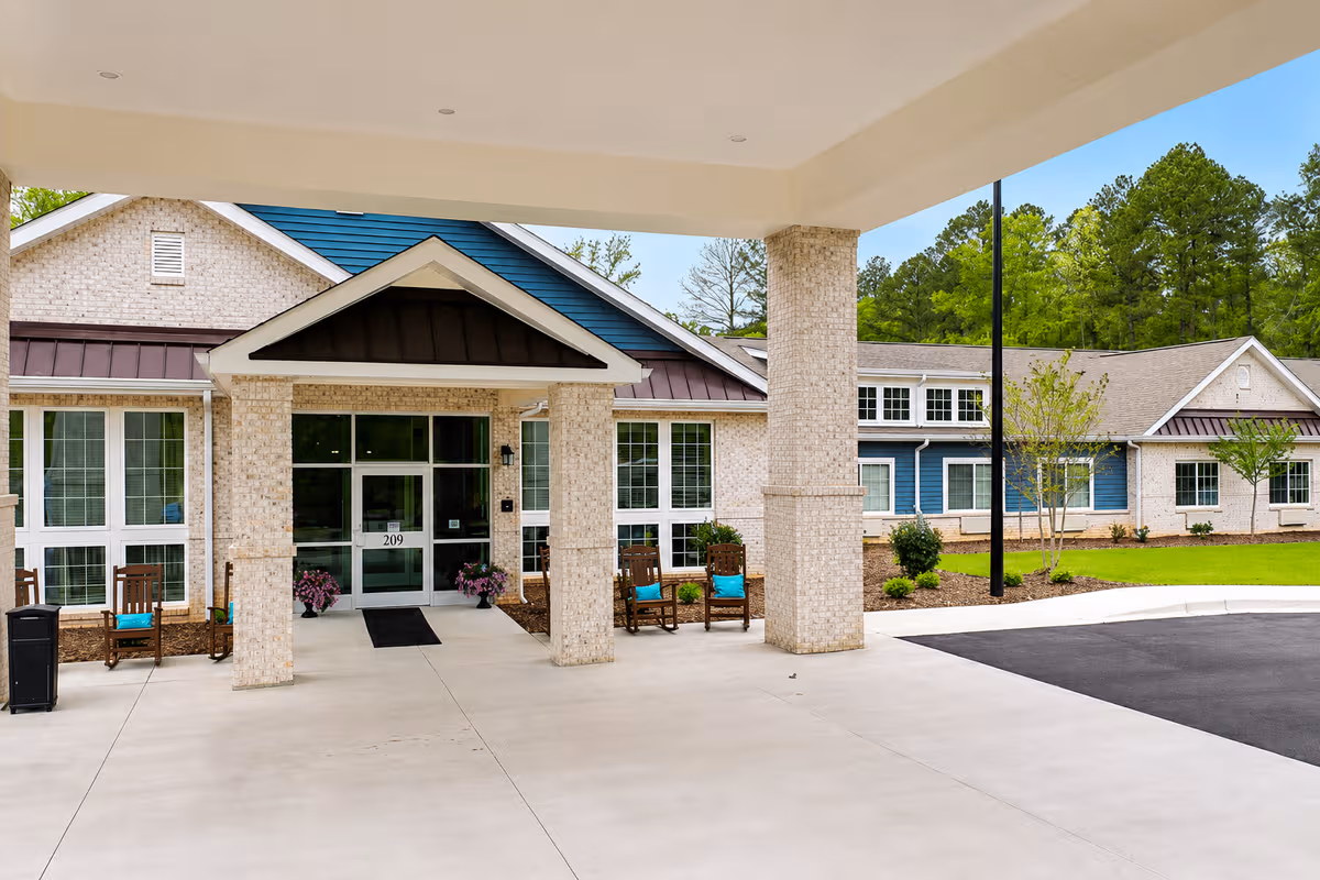 Front entrance of a senior living facility with a covered drop-off and seating.