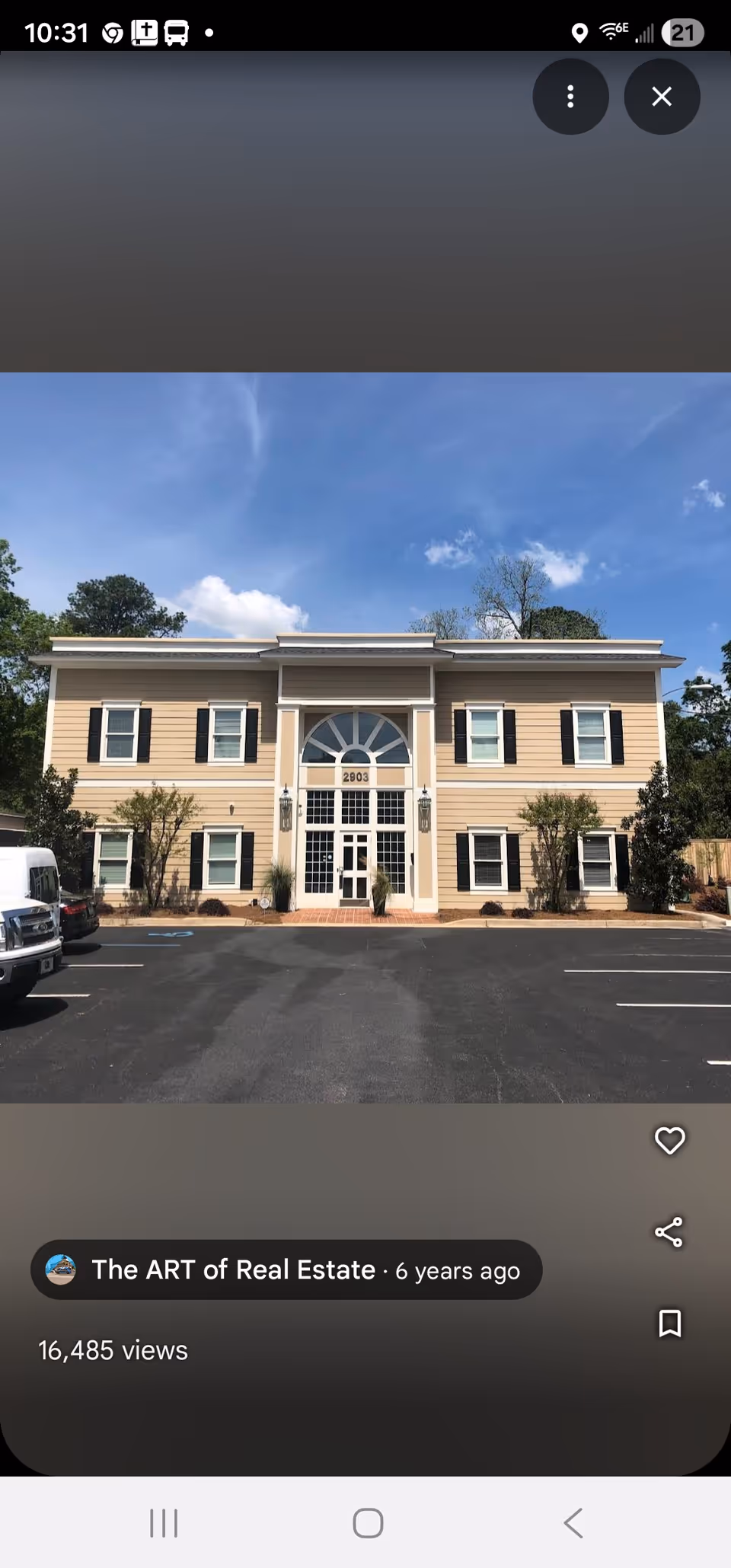 Front view of a beige, two-story senior care building with an arched entry and parking lot.