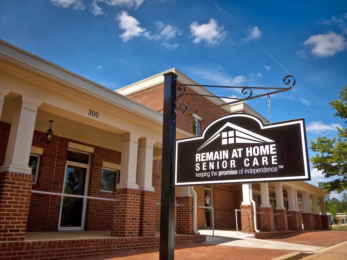 Brick building exterior with a large hanging sign reading Remain At Home Senior Care.