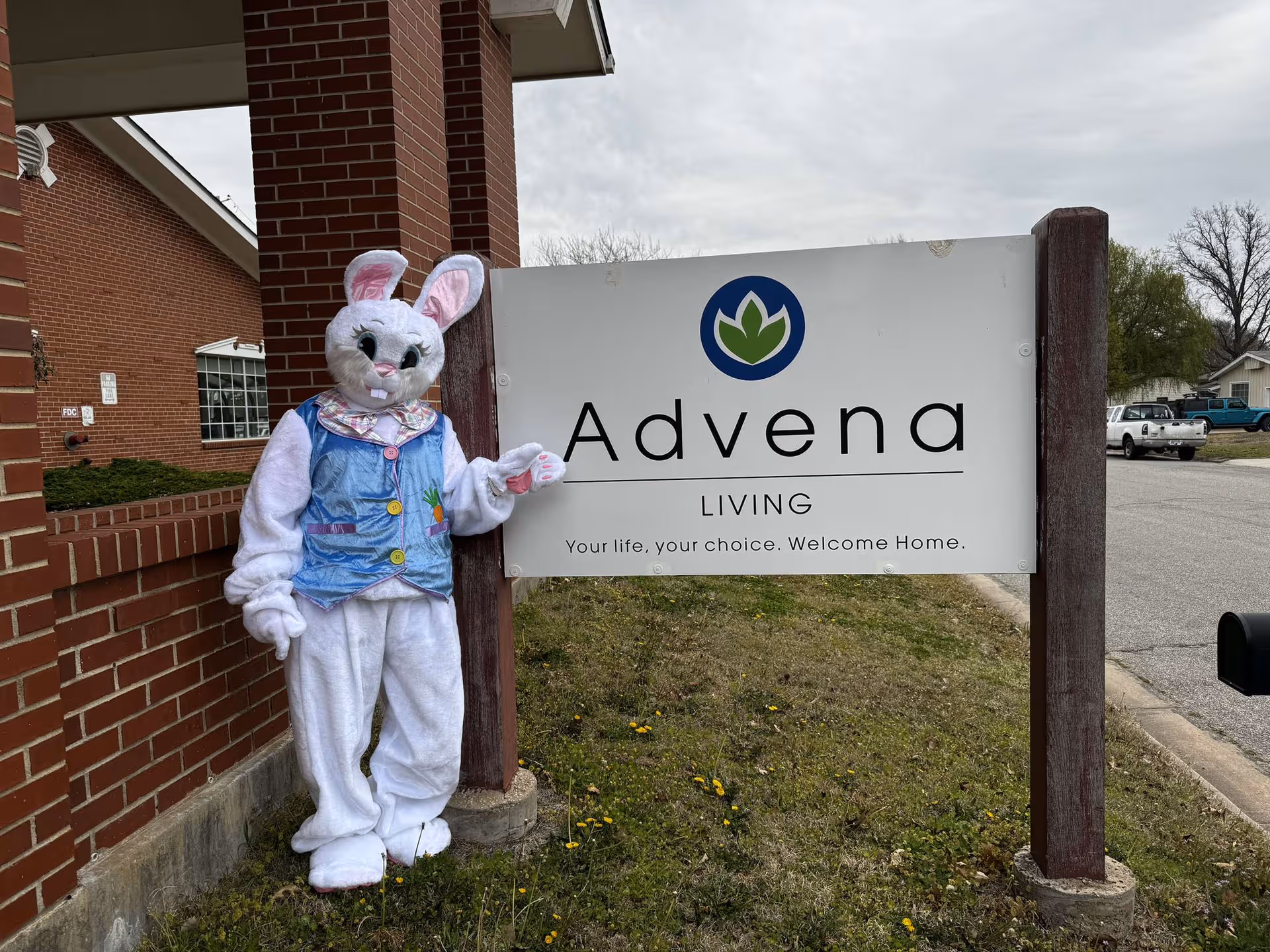 A bunny mascot stands beside an Advena Living sign outside a brick facility.