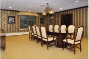 A formal dining room with a long wooden table, upholstered chairs, and patterned wallpaper.