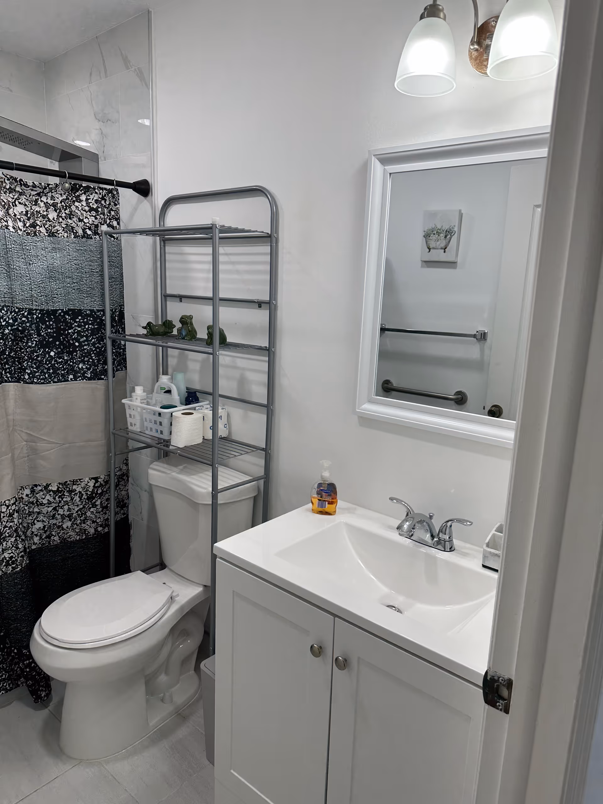 Compact bathroom with toilet, sink, mirror, shower curtain, and metal shelving unit.
