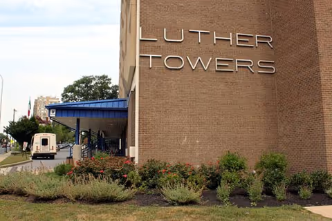Exterior view of Luther Towers building with blue awning and landscaped shrubs.
