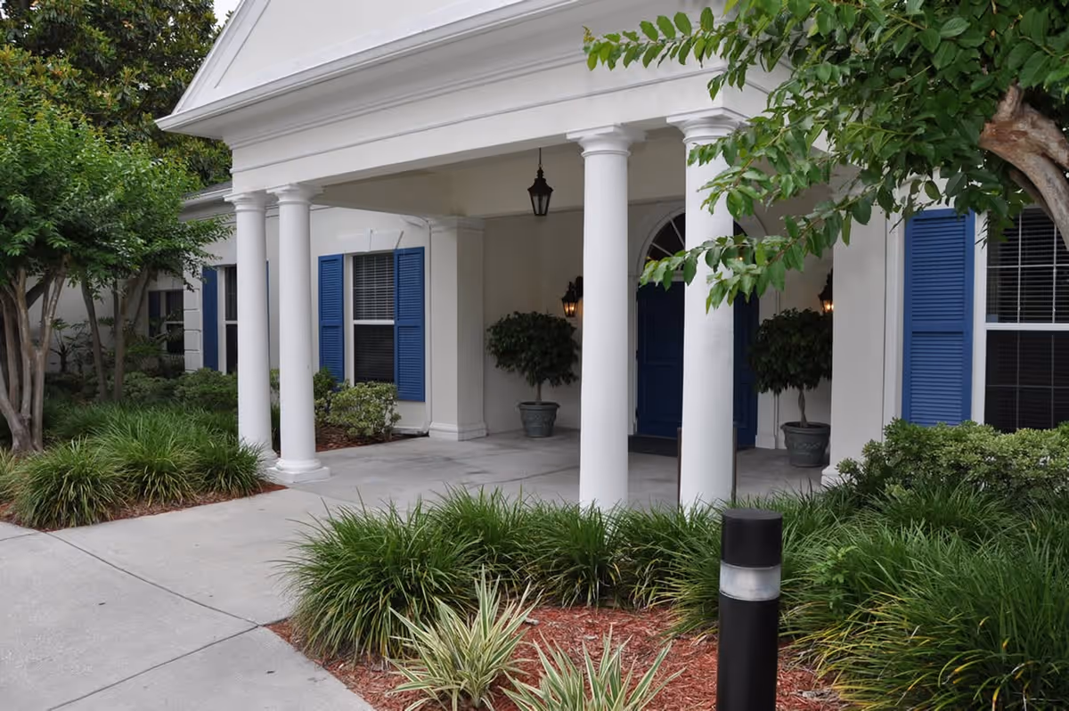Exterior view of a white building entrance with blue shutters and landscaped front yard.