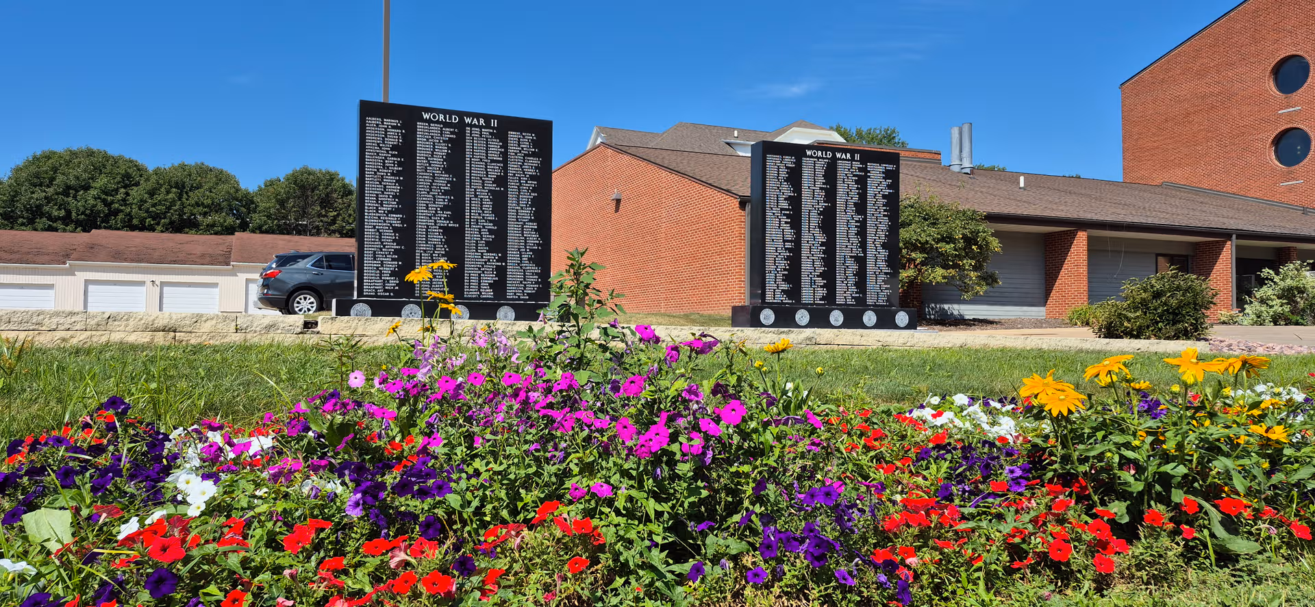 Exterior view of a senior facility with memorial boards and a colorful flower bed.