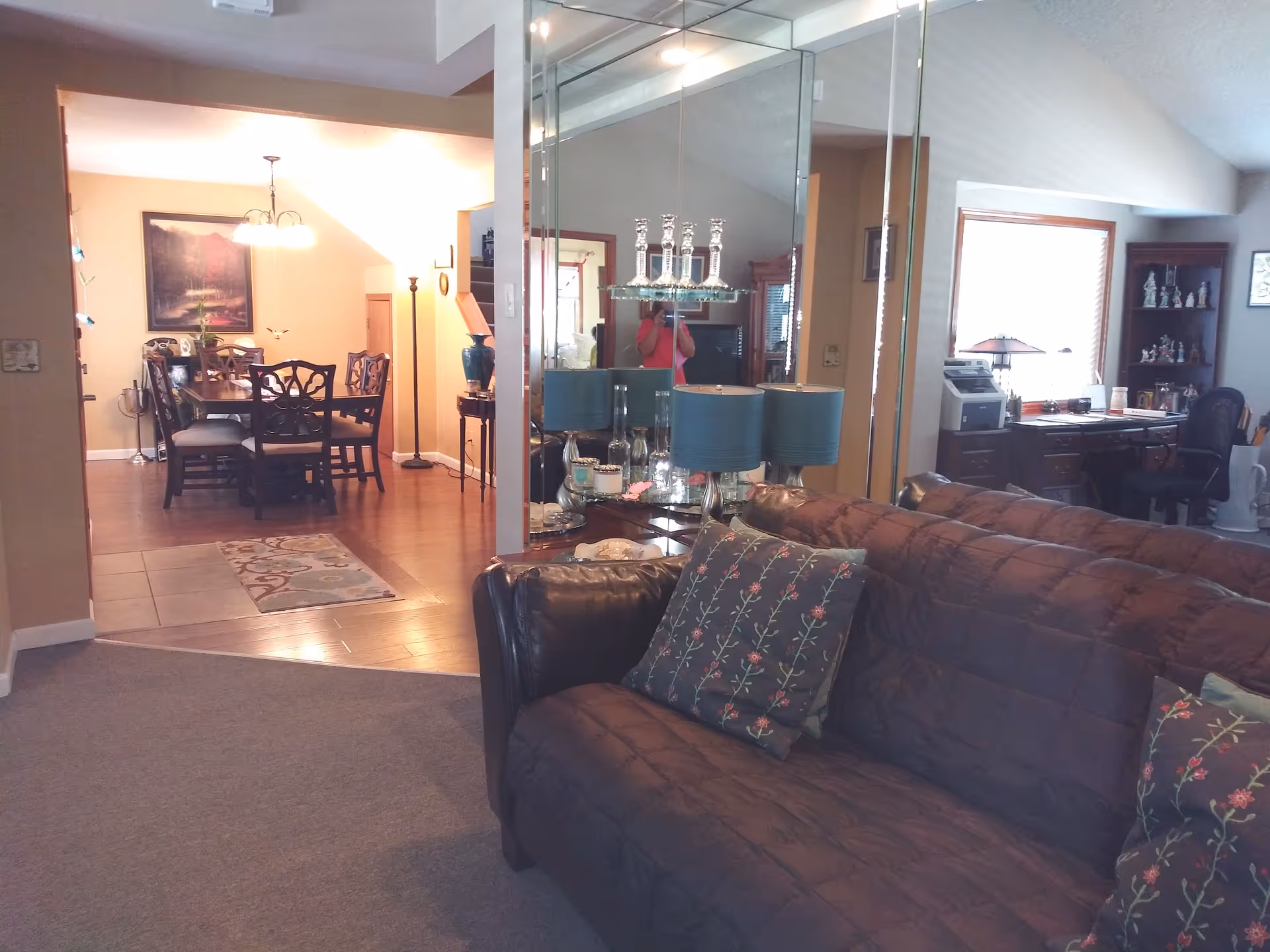 Cozy living room with brown sofa, mirrored divider, and dining area in background.