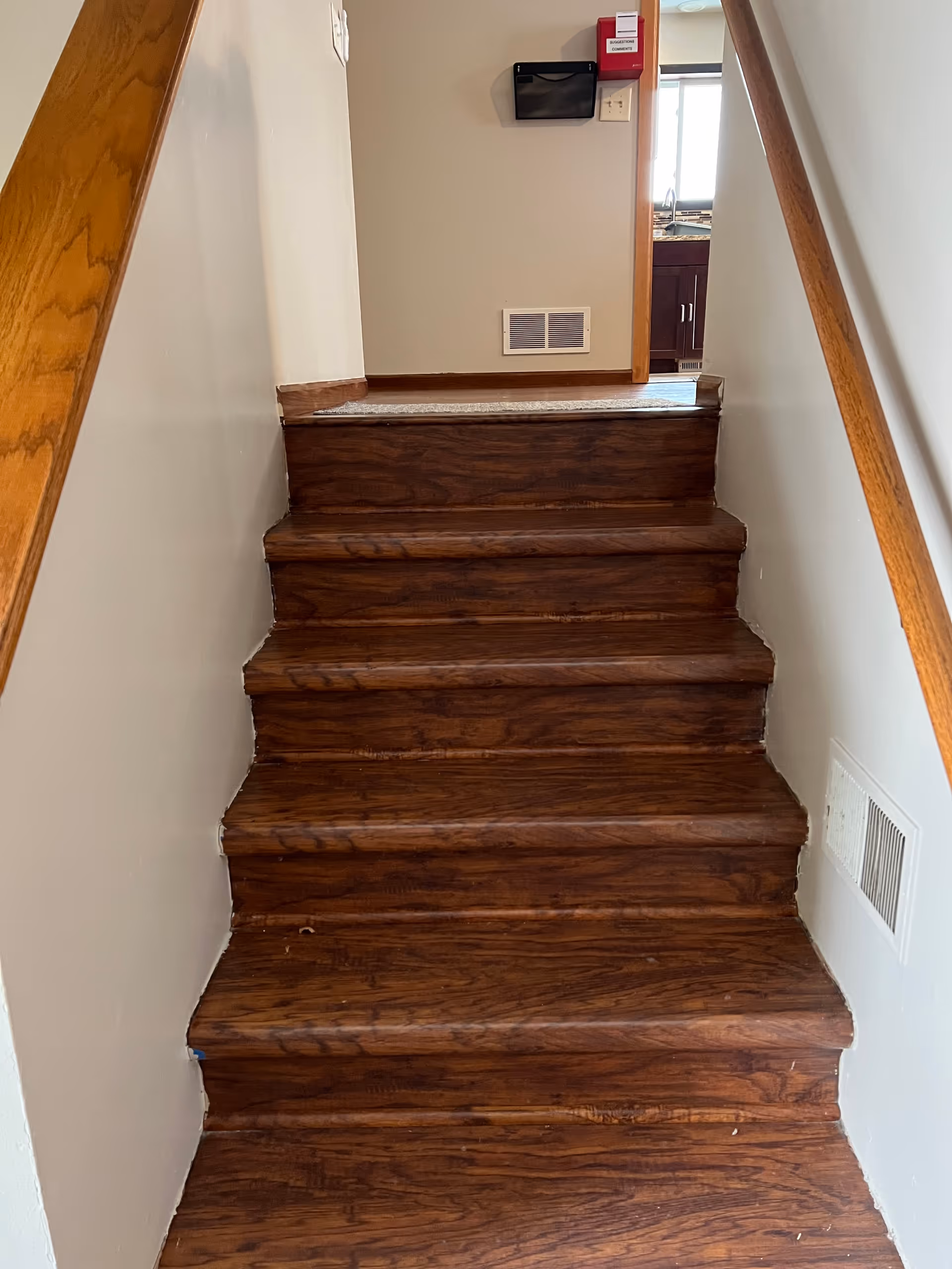 Wooden indoor staircase with railings leading to a doorway and visible kitchen.