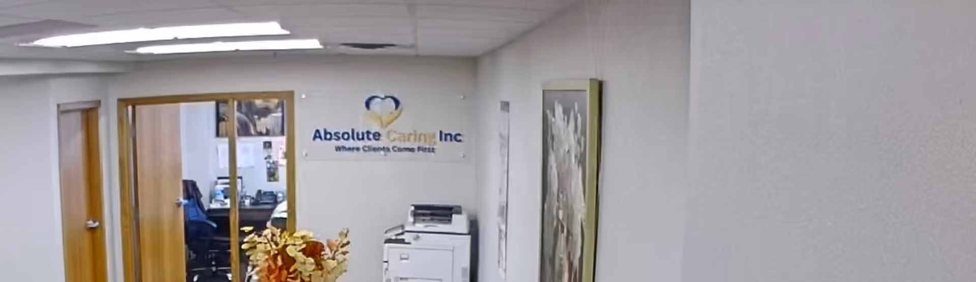 Interior hallway of Absolute Caring Inc with sign, doorway to offices, and office equipment