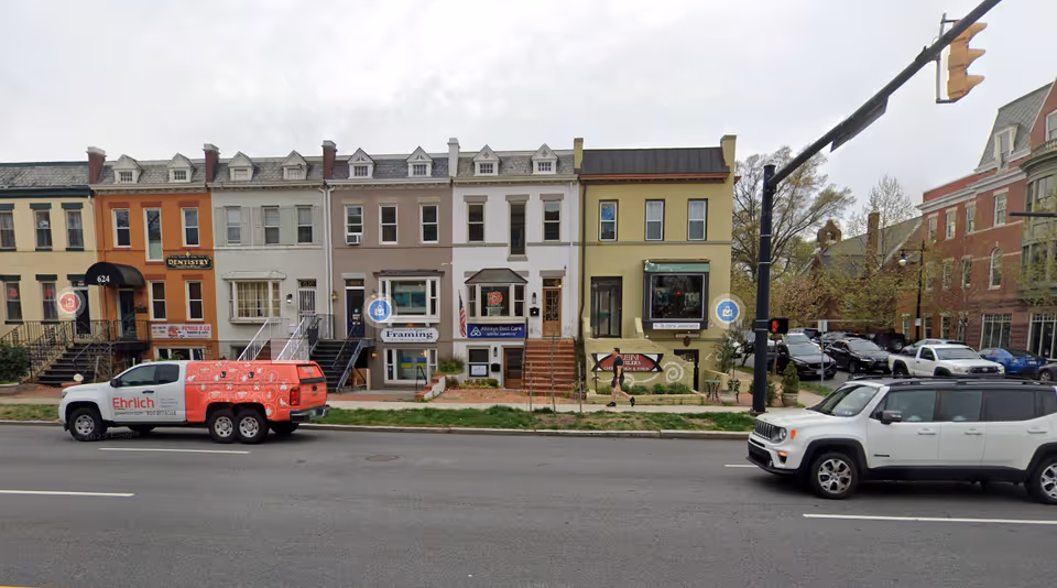 Row of colorful storefront buildings on a busy street with parked cars.