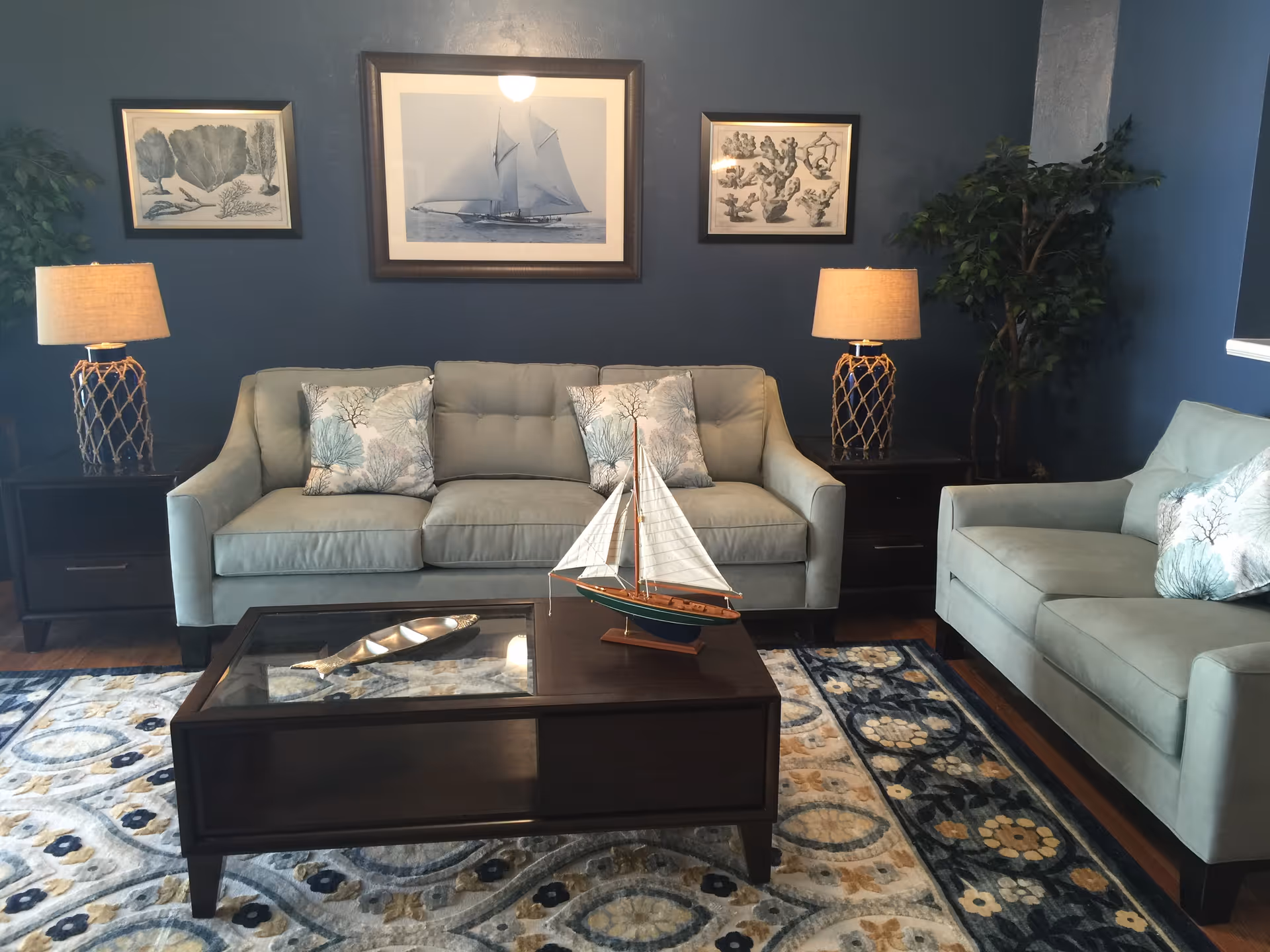 Blue-toned living room with matching sofas, a coffee table, lamps, and wall art.
