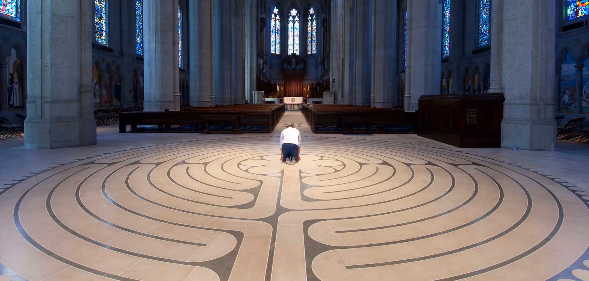 Person kneels at center of circular labyrinth inside a cathedral.