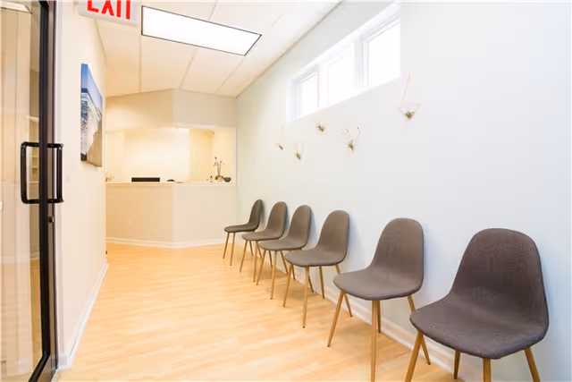 Waiting area with gray chairs along a light blue wall and a reception desk.