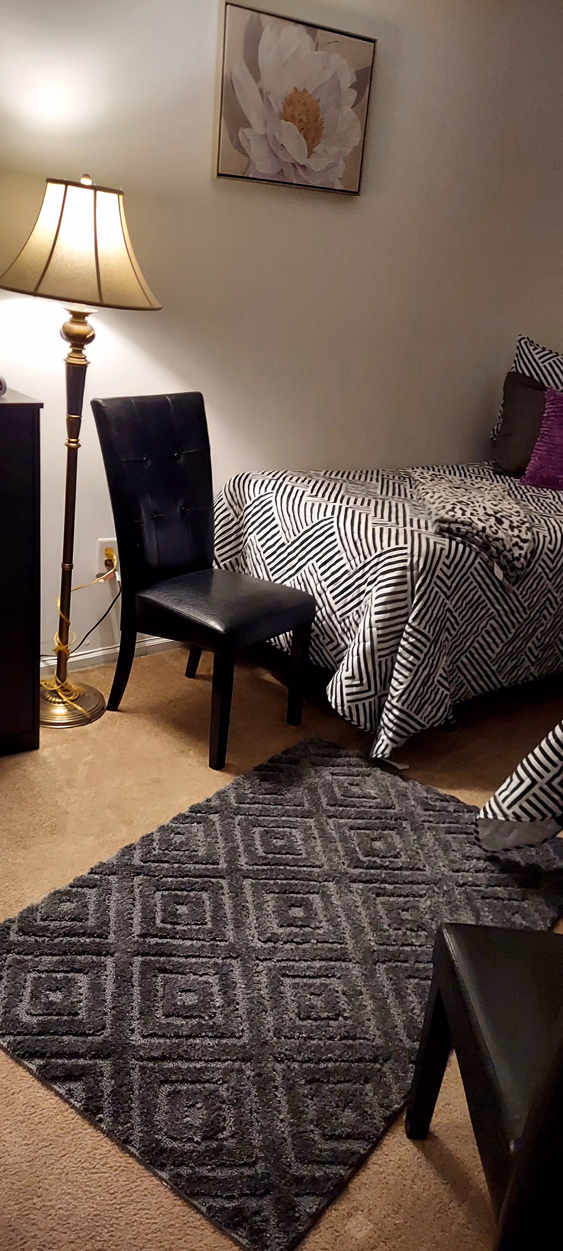 Bedroom with bed, chair, lamp, geometric rug, and framed floral art.