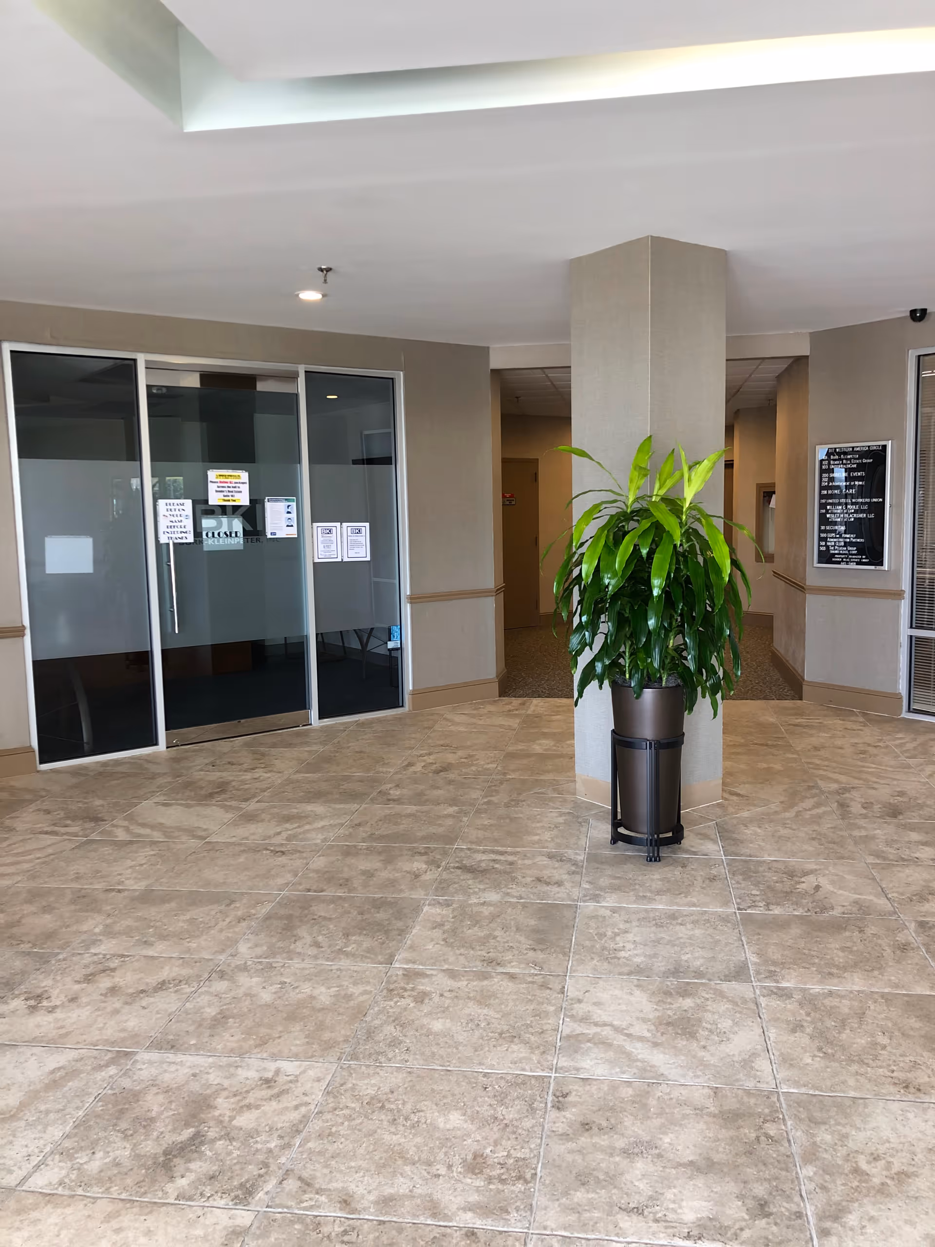Lobby area of a seniors facility with glass doors, a large potted plant, and tiled floor.
