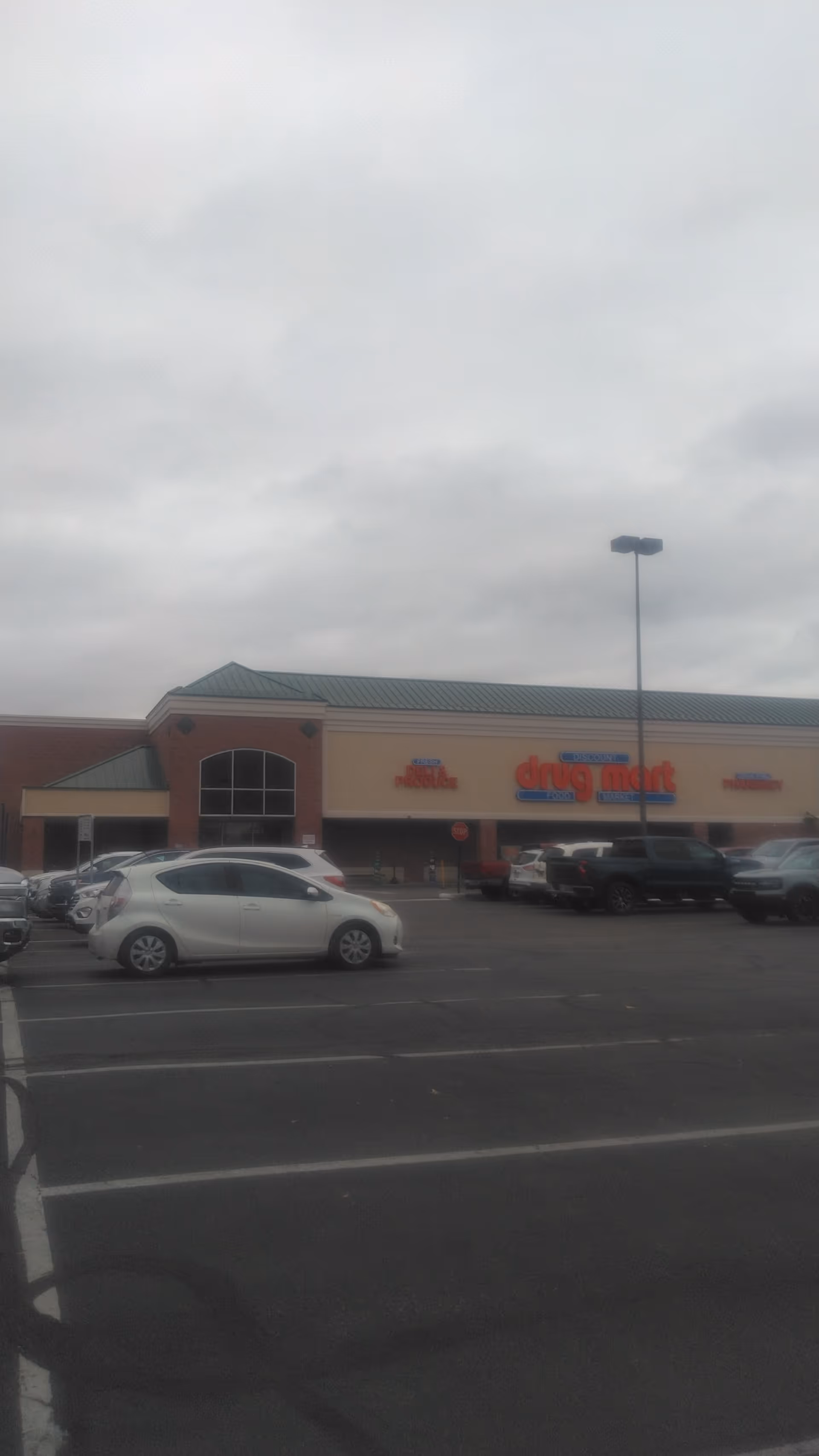 Exterior view of Discount Drug Mart storefront with parked cars in a parking lot.