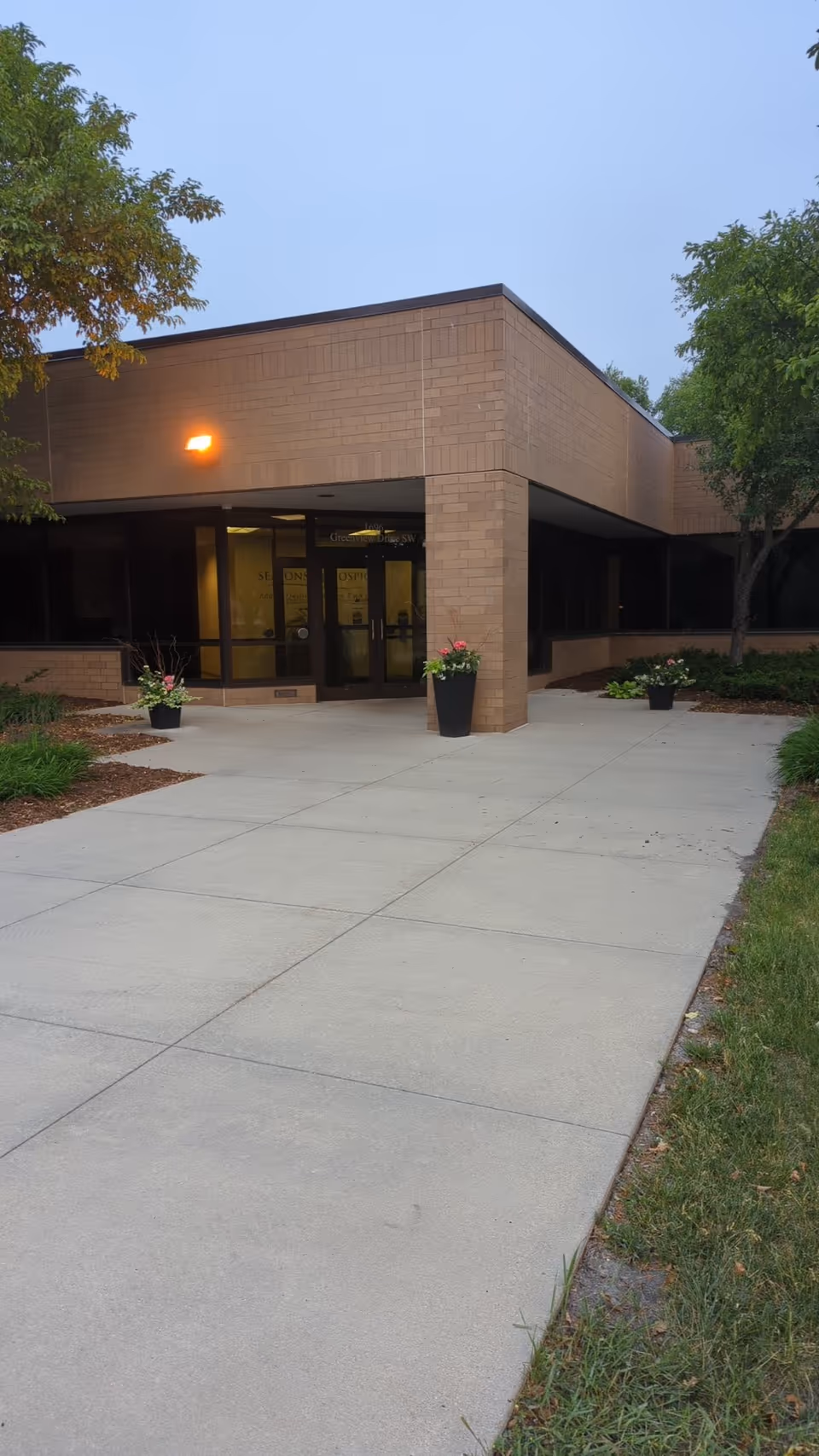 Exterior view of Seasons Hospice entrance with brick building and concrete walkway.