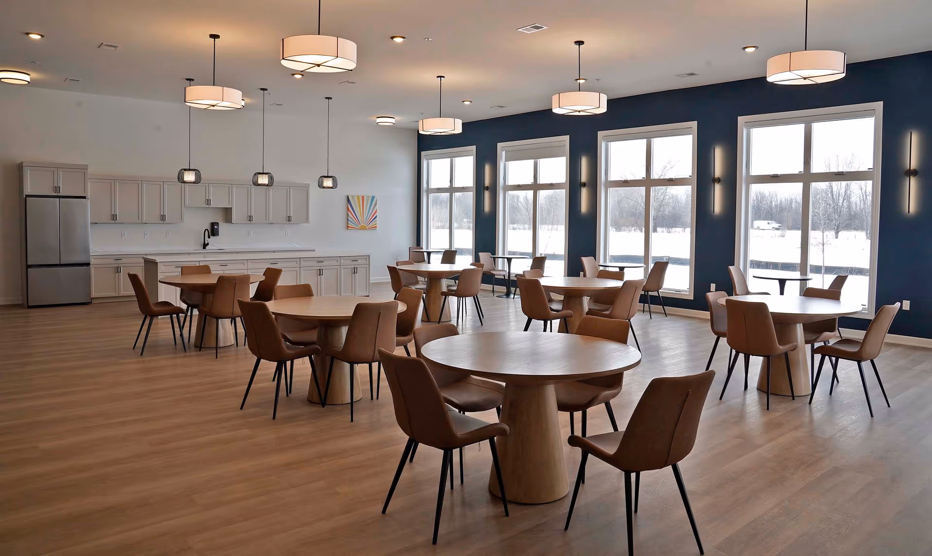 Open dining area with round tables, tan chairs, and a white kitchen along the back wall.