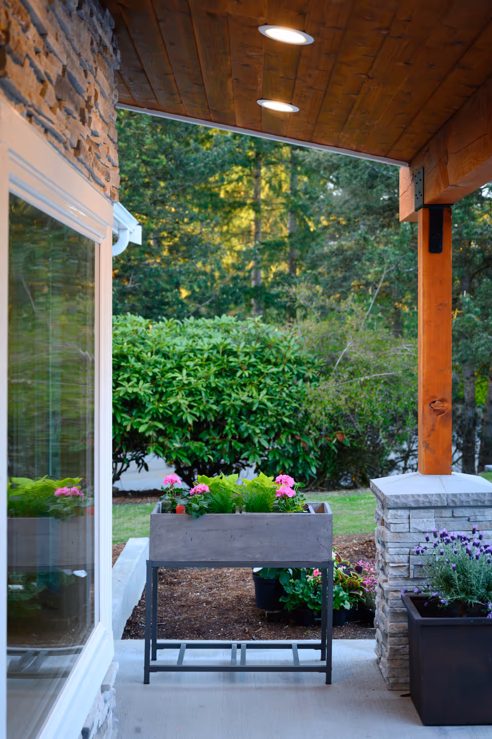 Outdoor porch with planters, greenery, wood ceiling, and a stone column.